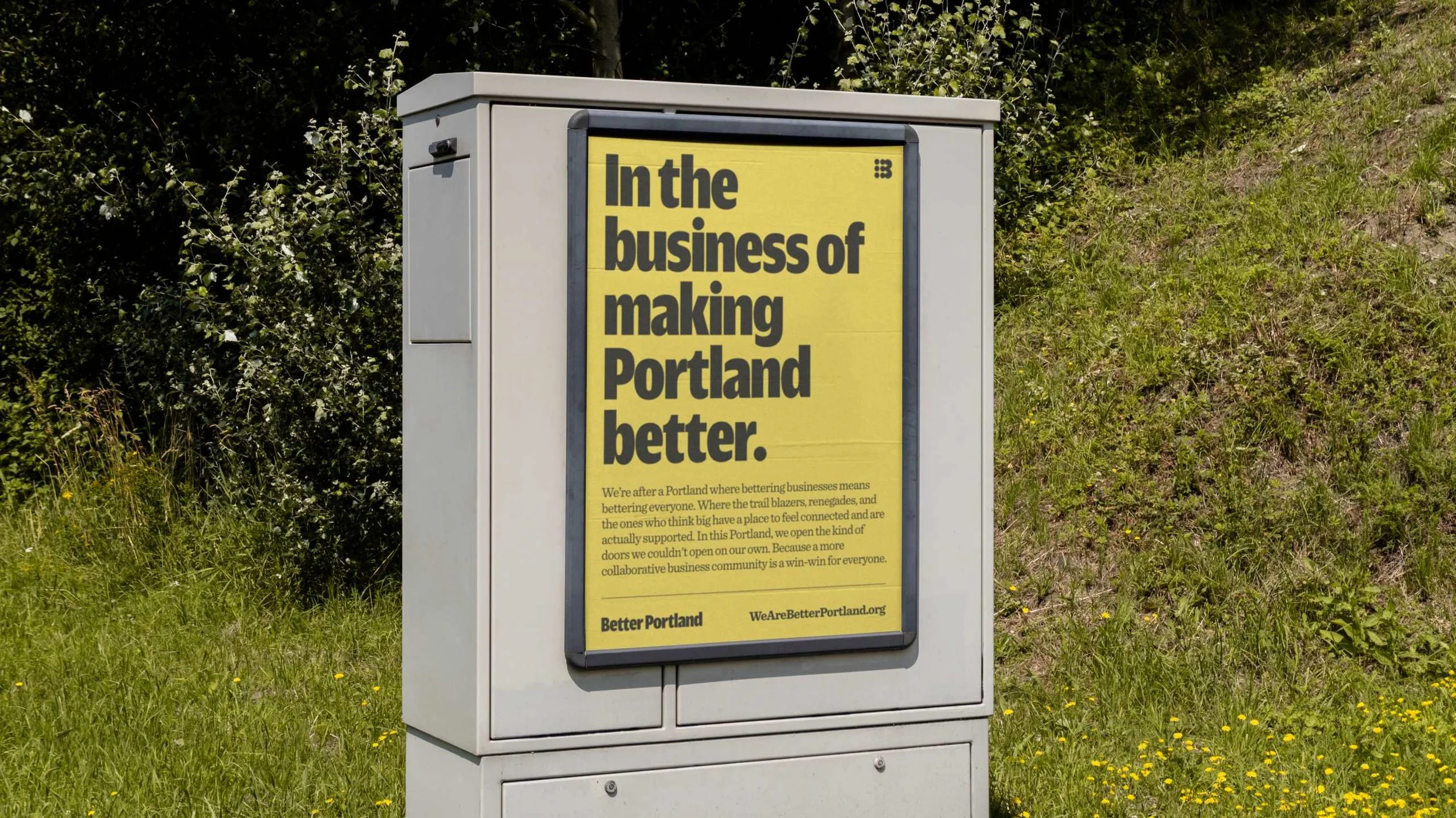 A yellow sign on a gray utility box reads: 'In the business of making Portland better.' Additional text explains supporting local businesses and community collaboration, with the website BetterPortland.org.