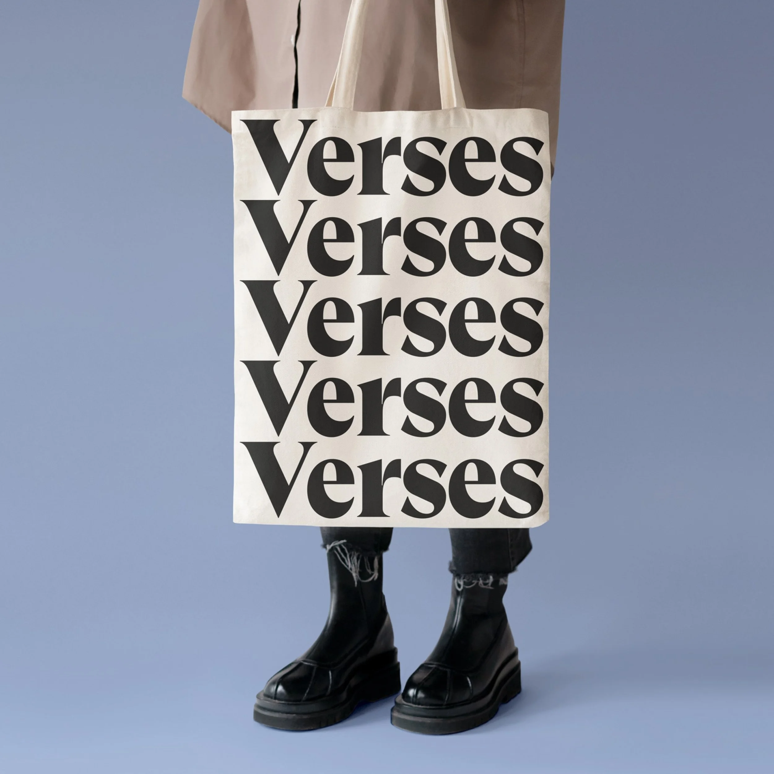 Person wearing black boots and ripped jeans holding a tote bag with the word 'verses' repeated multiple times in bold black letters on a white background.