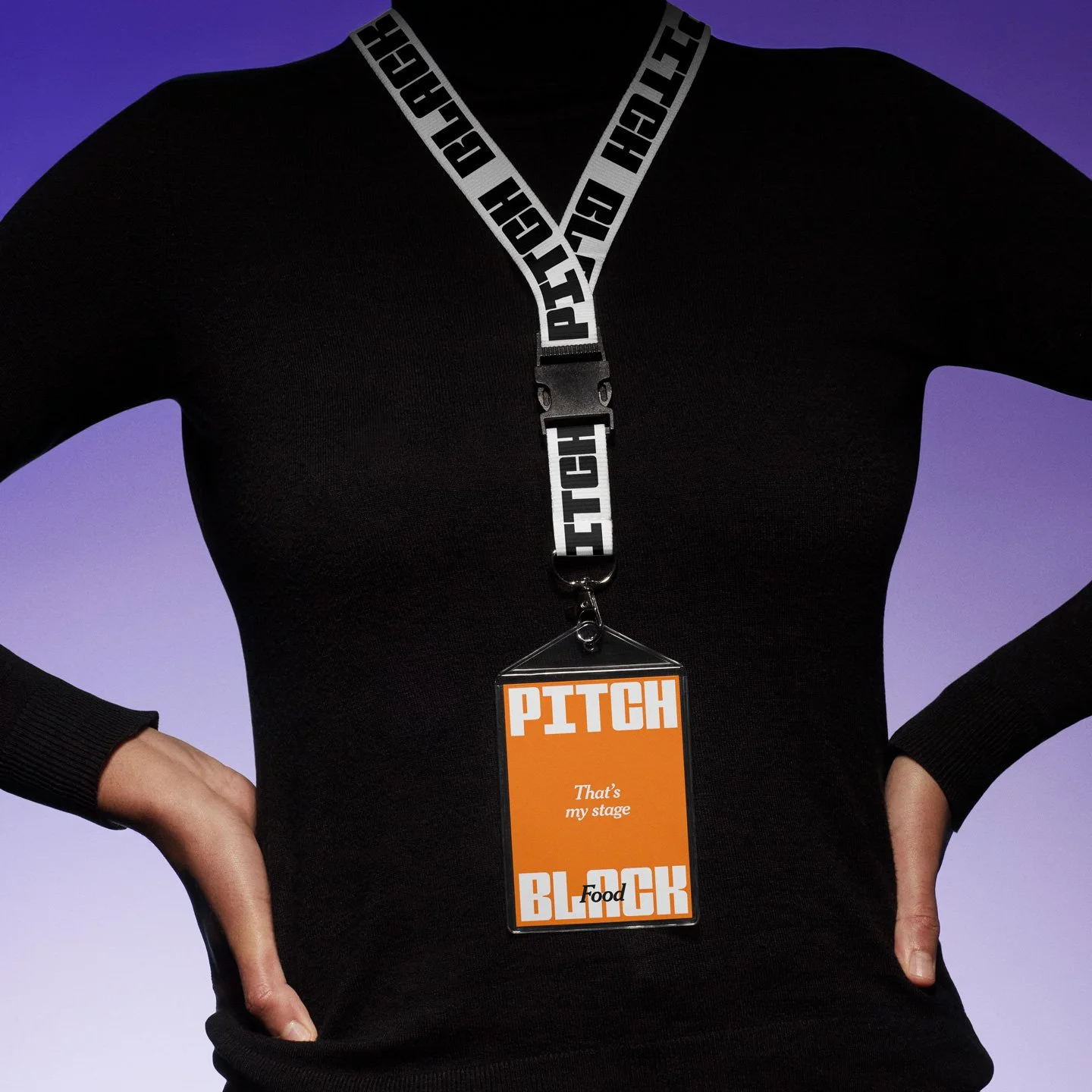 Person wearing a black long-sleeve shirt with hands on hips, with a lanyard around neck and a badge that reads "PITCH" and "That's my stage" and "FOOD".