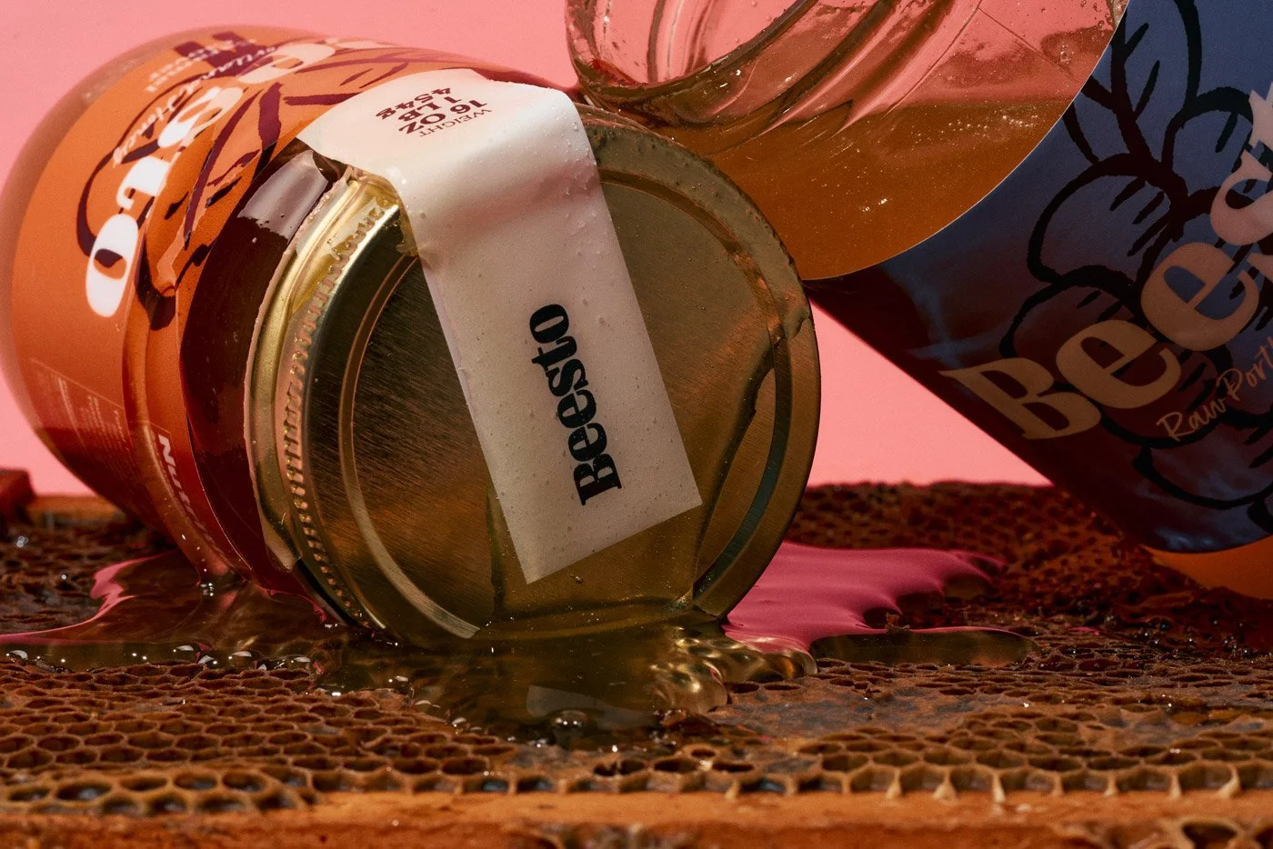 A spilled jar of honey labeled "Beasto" and a bag of beef jerky on a textured surface with honey liquid and honeycomb.