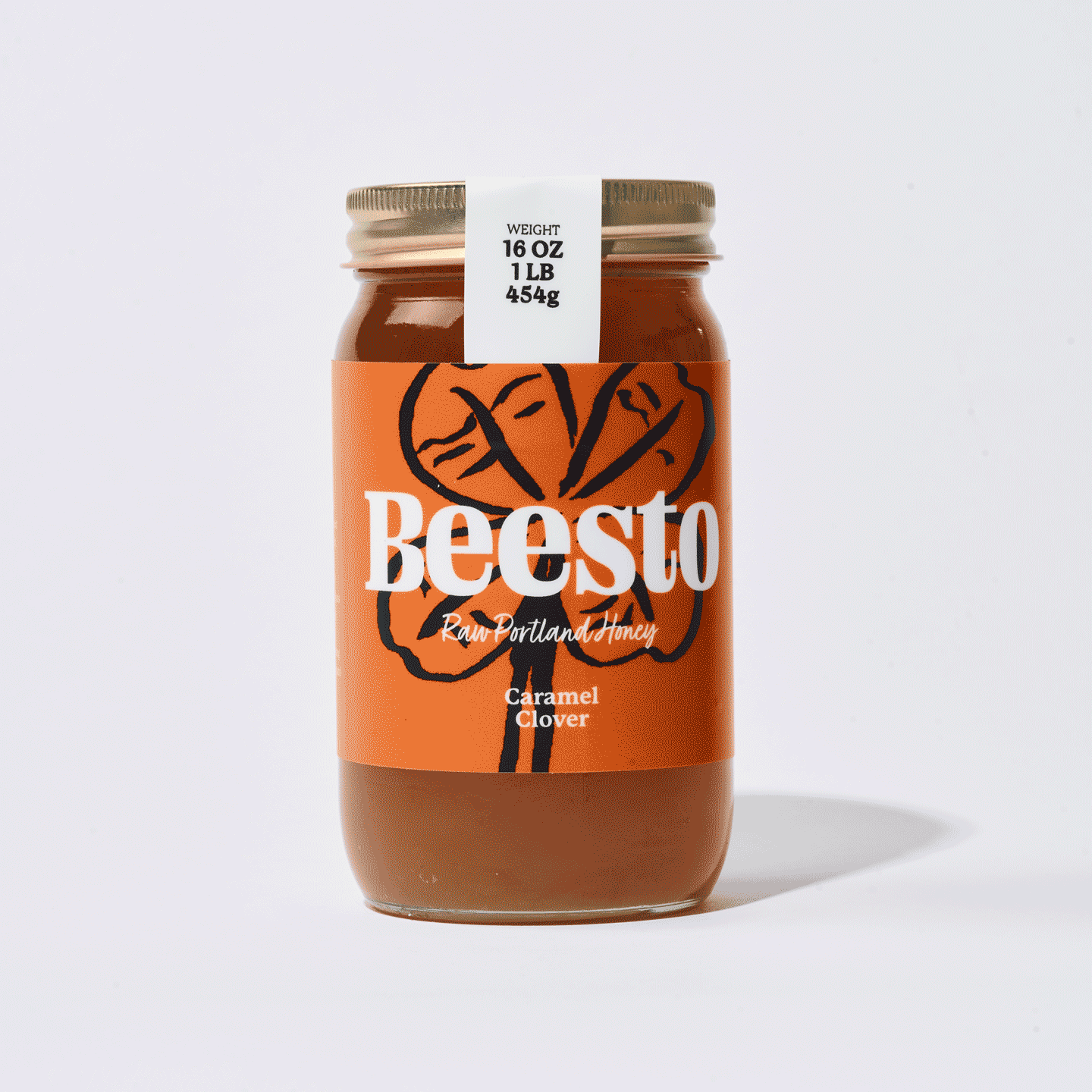 A jar of Beesto caramel clover honey with a white label on the lid indicating weight, set against a plain white background.
