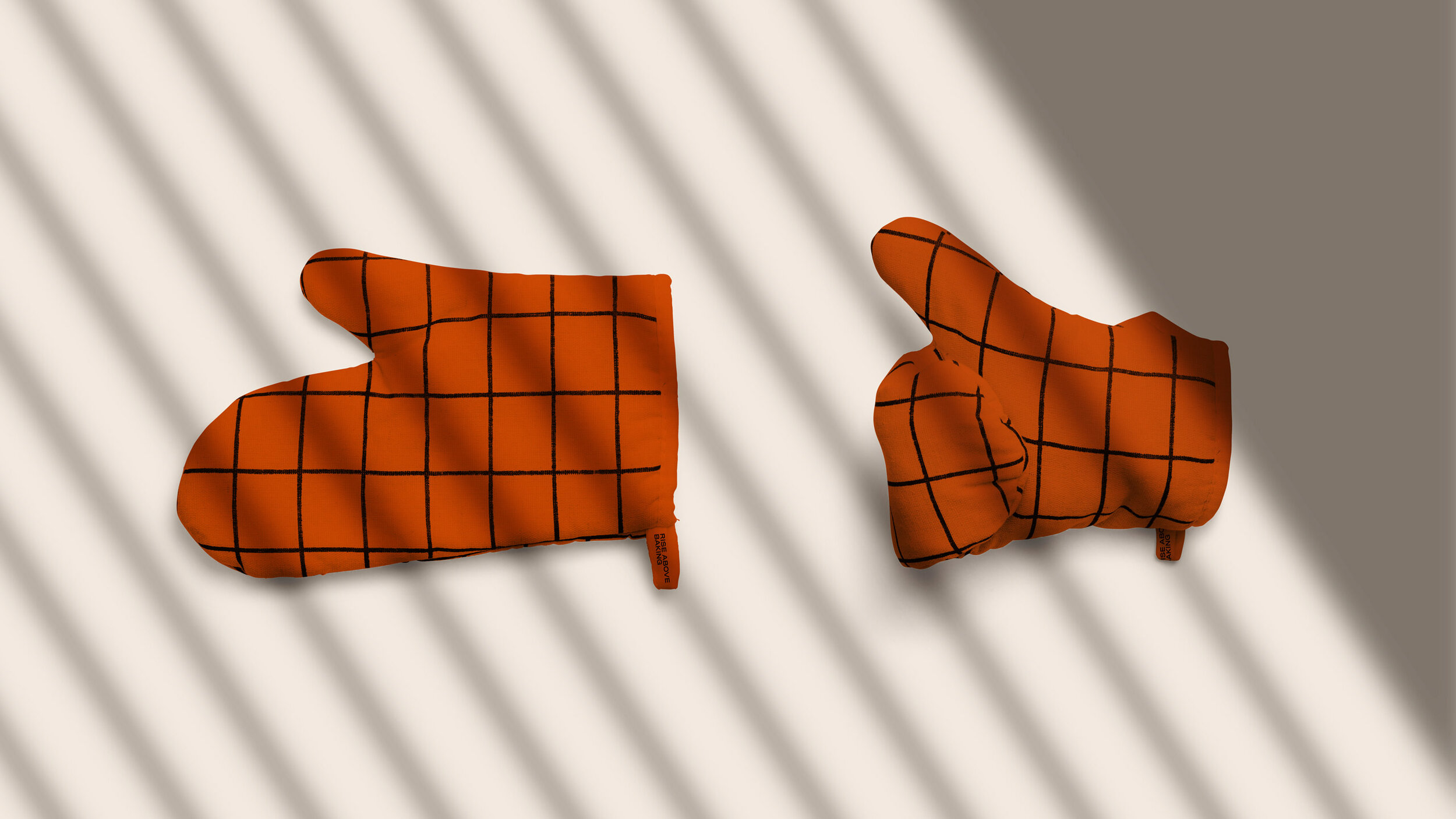 Orange oven mitt with black grid pattern lying on a white surface with diagonal shadows.