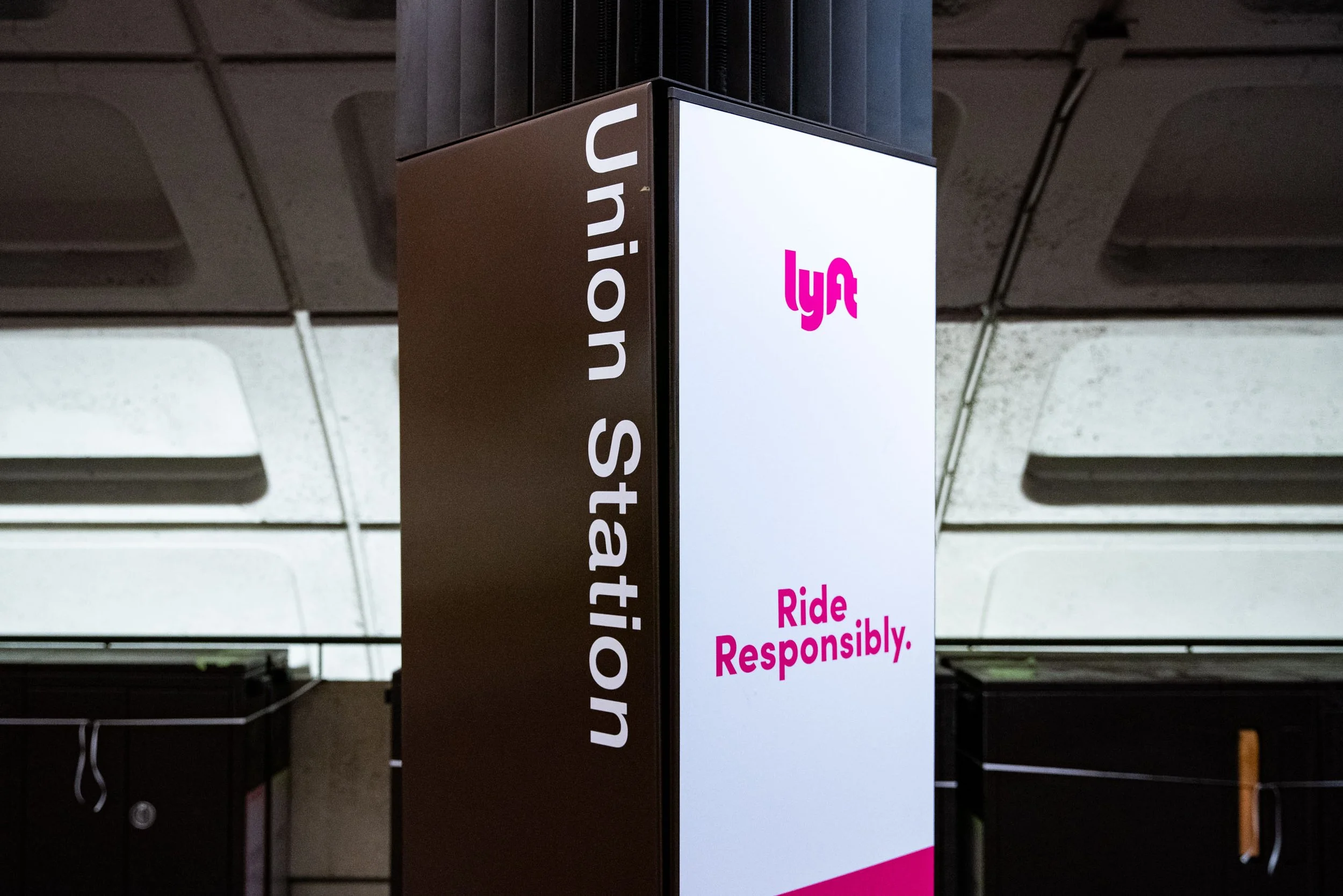 Sign with Lyft logo and message about riding responsibly, located on a wall or pillar at a transportation station.