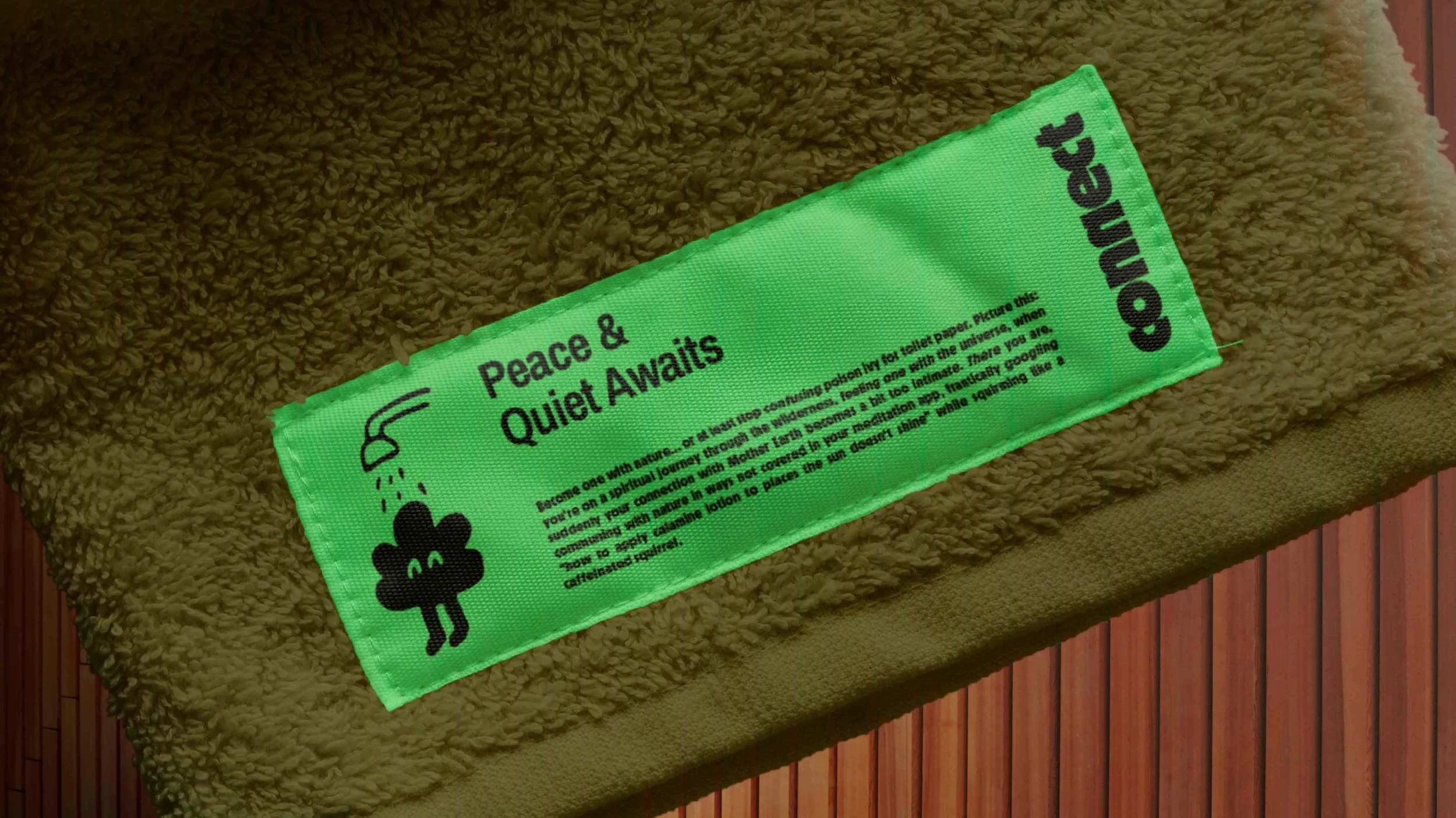 A green towel with a label that says 'Peace & Quiet Awaits,' lying on a textured brown towel on a wooden surface.