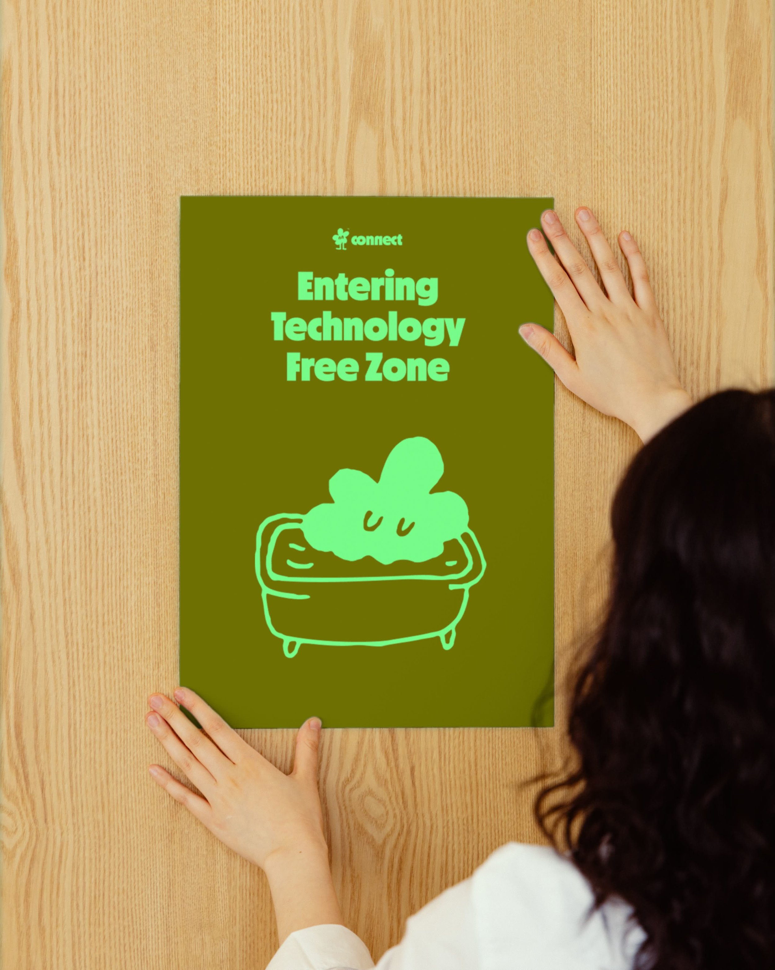 A person with long dark hair is placing their left hand on a green poster board that says 'connect' and 'Entering Technology Free Zone' with a drawing of a happy, steaming bowl of food.