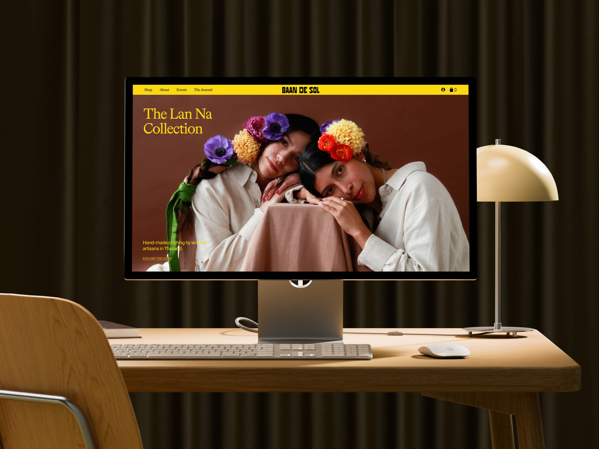 Computer monitor on a wooden desk displaying a website with a woman and girl wearing flower crowns, with a yellow header and brown background.
