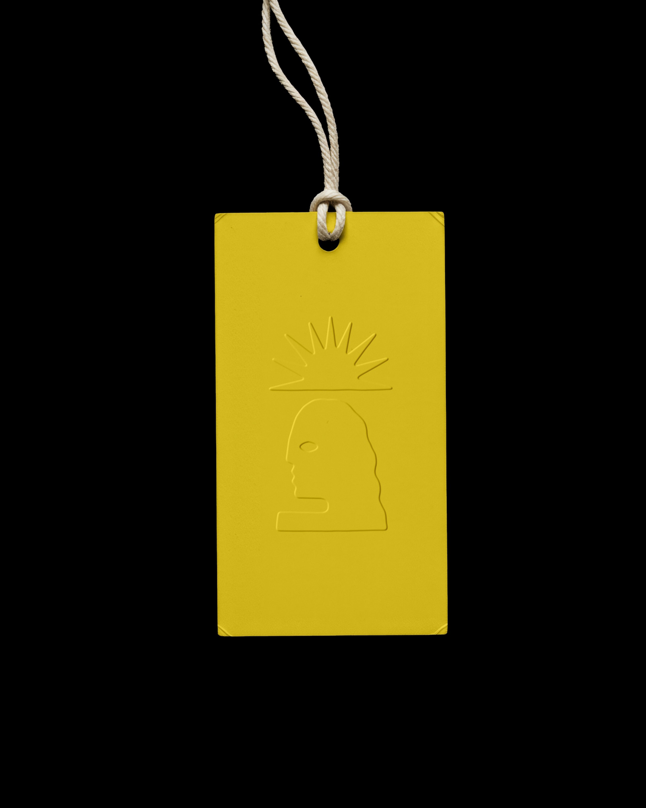 Yellow rectangular tag with a white string tied through a hole at the top, featuring an embossed illustration of a human profile with a radiating sunburst pattern above the head, set against a black background.