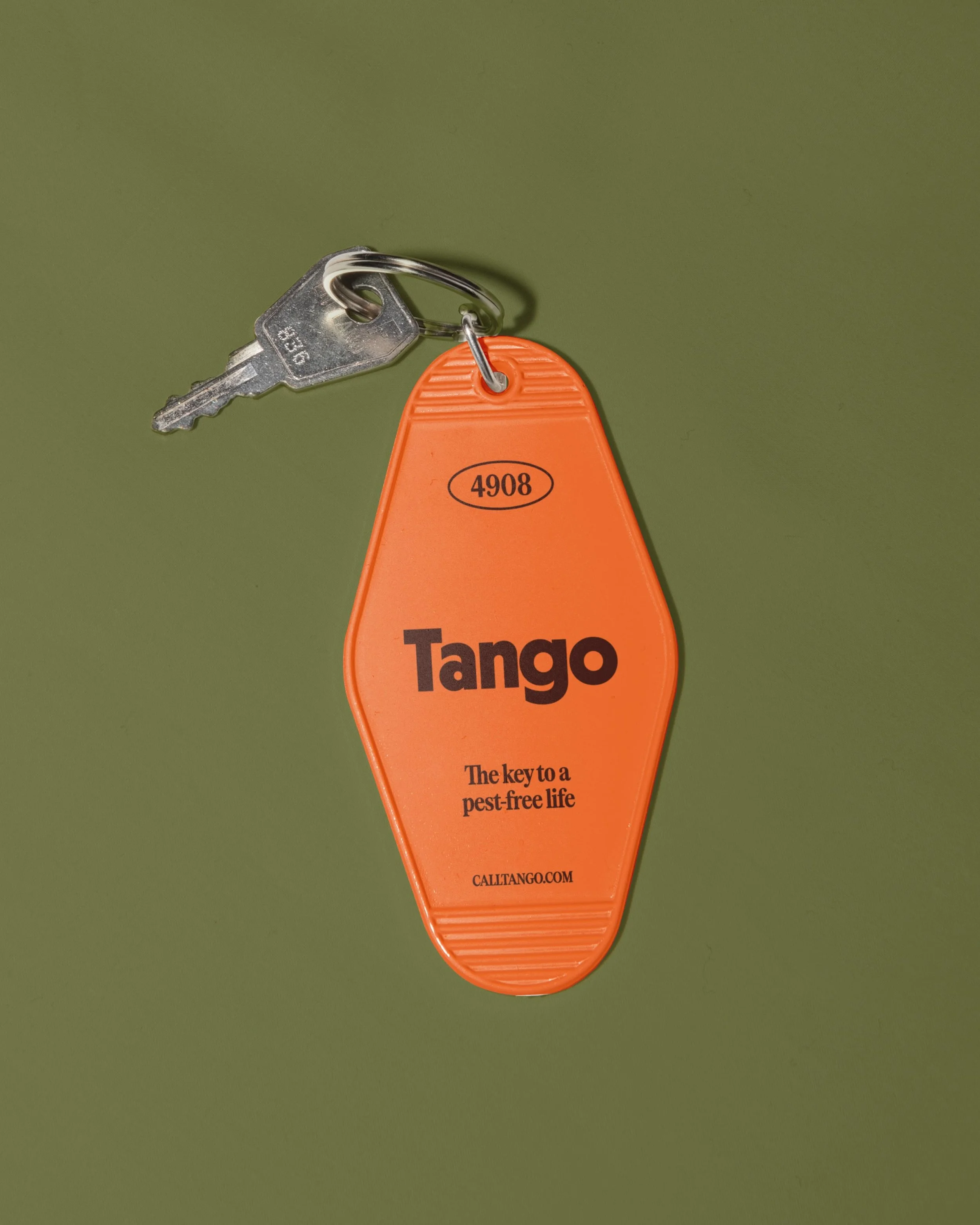 A close-up of a bright orange tag attached to a keyring with a silver key, placed against a green background. The tag reads "Tango" and has a slogan about pest control.