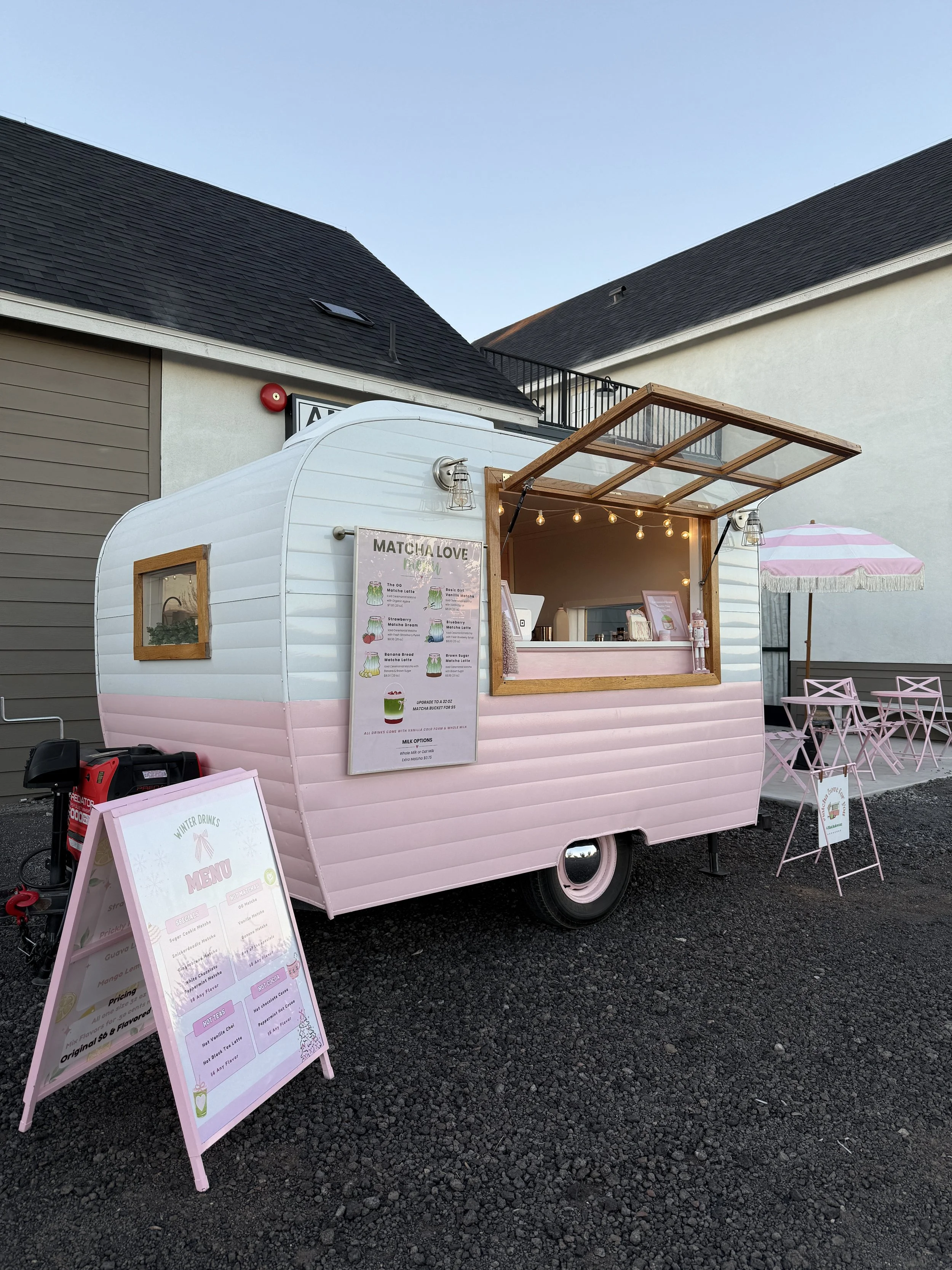 Pink and white ice cream or smoothie truck with menu boards, outdoor seating, and an umbrella.