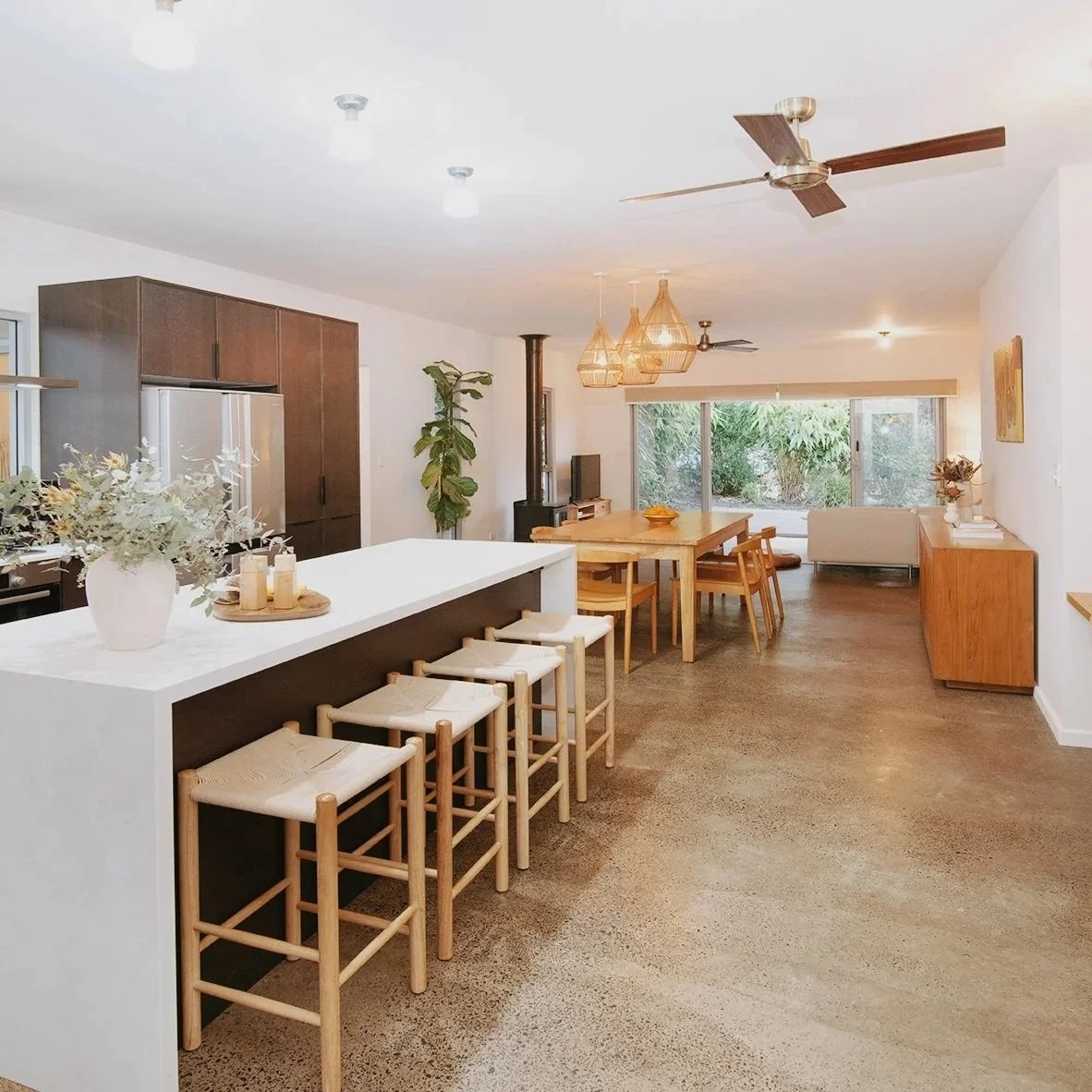 Open-plan kitchen and dining area styled for sale with oak stools, polished concrete floors, and natural textures — a cohesive, light-filled transformation.