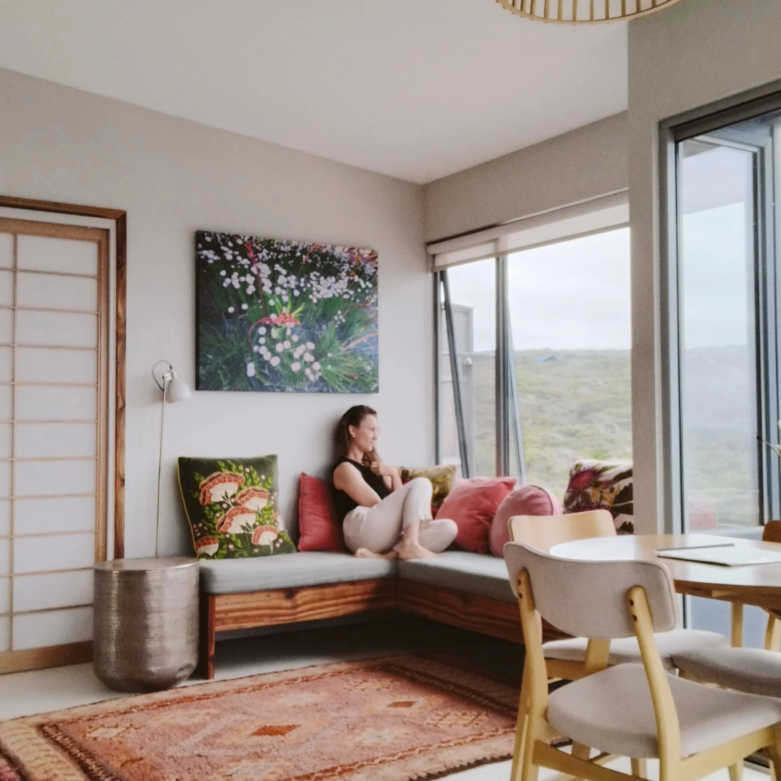 Coastal living room with natural timber, vintage rug, and ocean-view windows — serene, eco-luxury interior design inspired by boutique coastal simplicity.