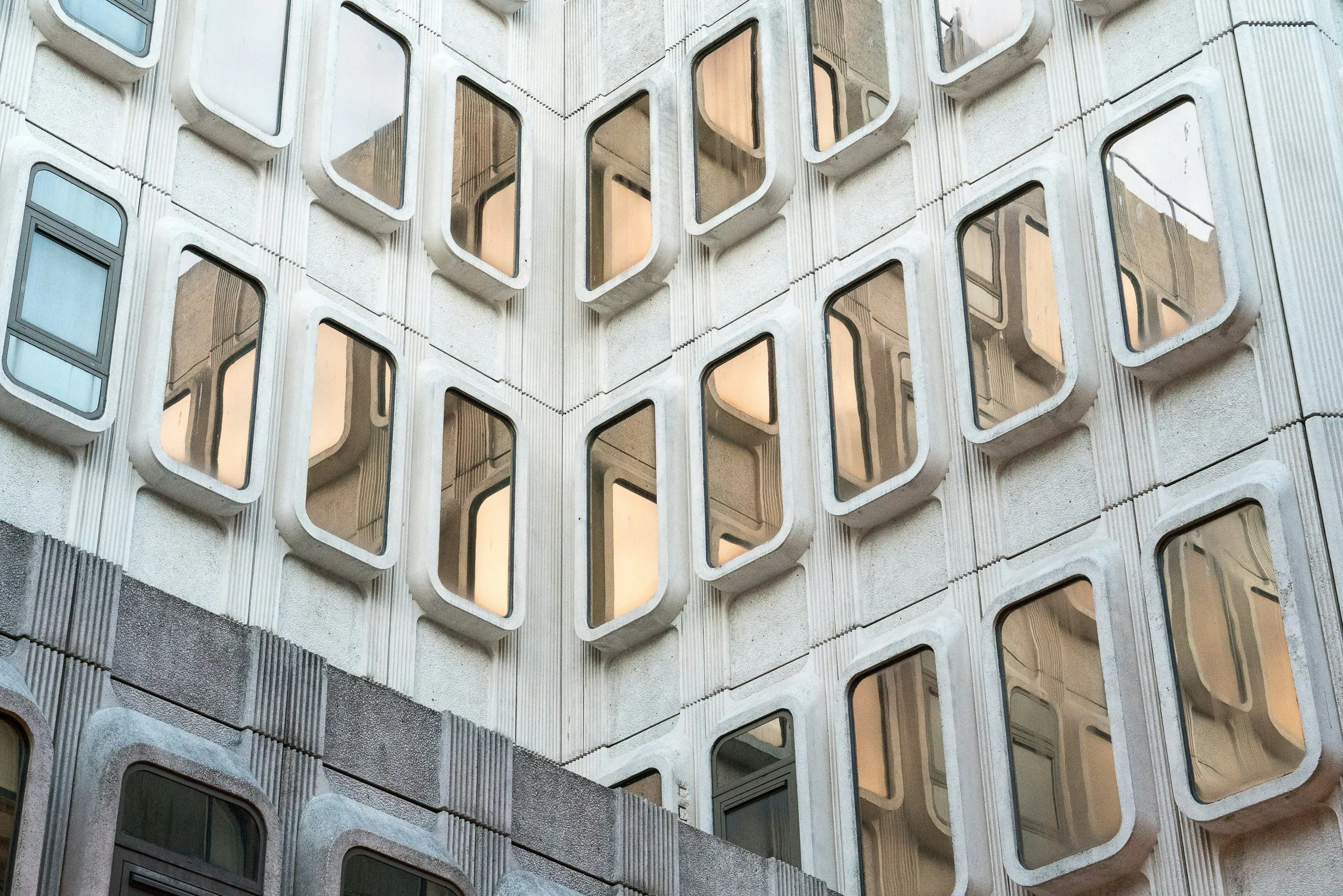 Close-up of a building facade with multiple rectangular windows framed by rounded concrete borders, arranged in a grid pattern.