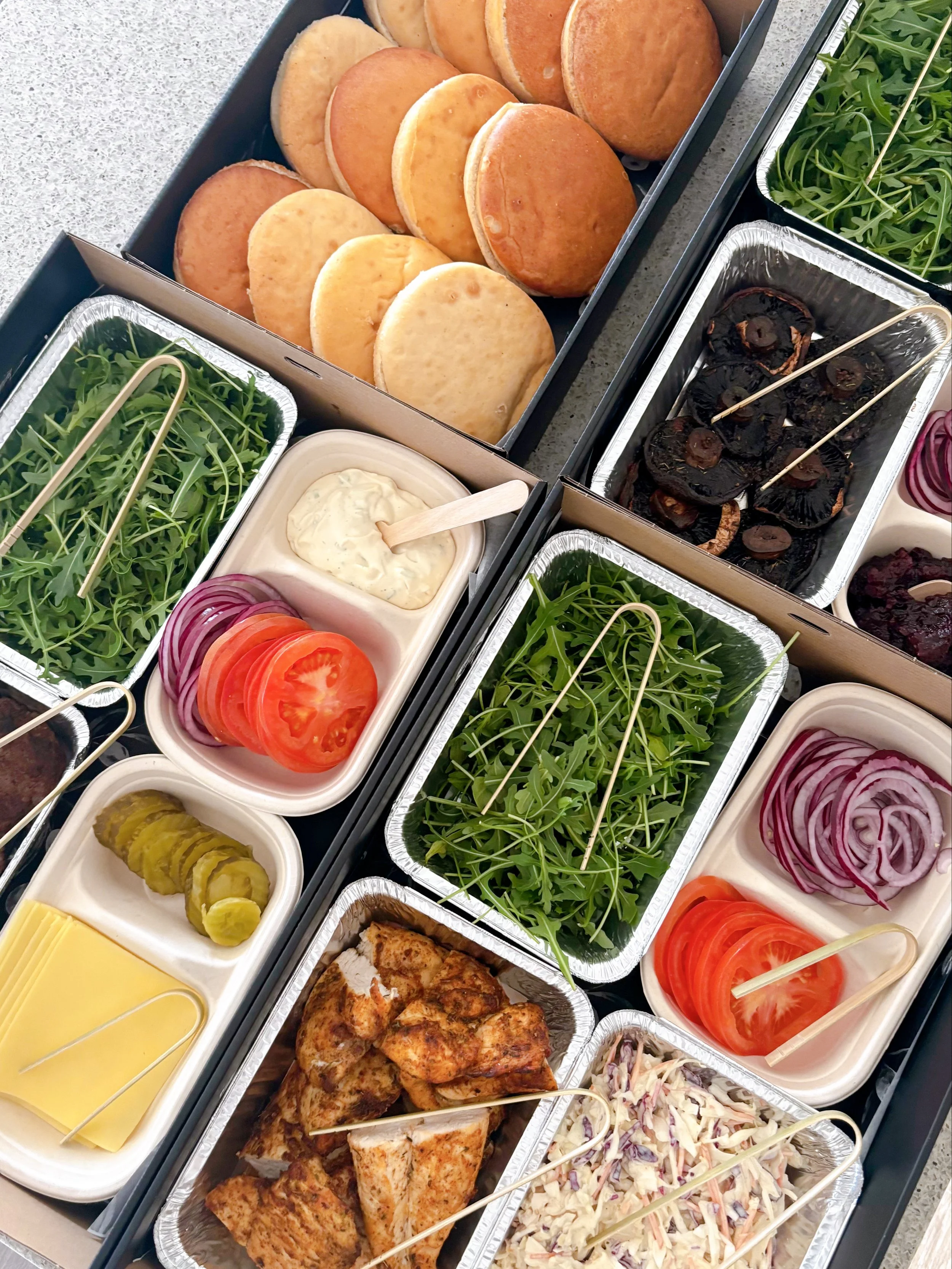 Boxed sandwiches, grilled chicken, salads, sliced tomatoes, sliced red onions, pickles, and greens.