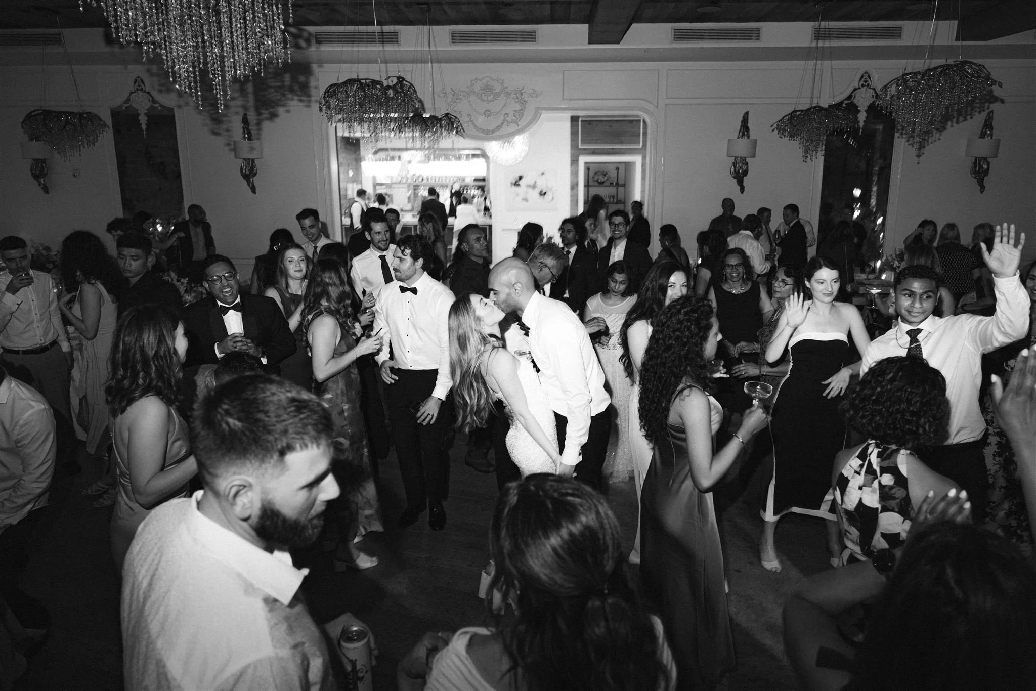 A crowded wedding reception with guests dancing and socializing inside a decorated hall.