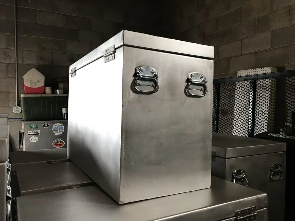 Stainless steel container with metal handles on a work surface in a kitchen setting, with a brick wall background.