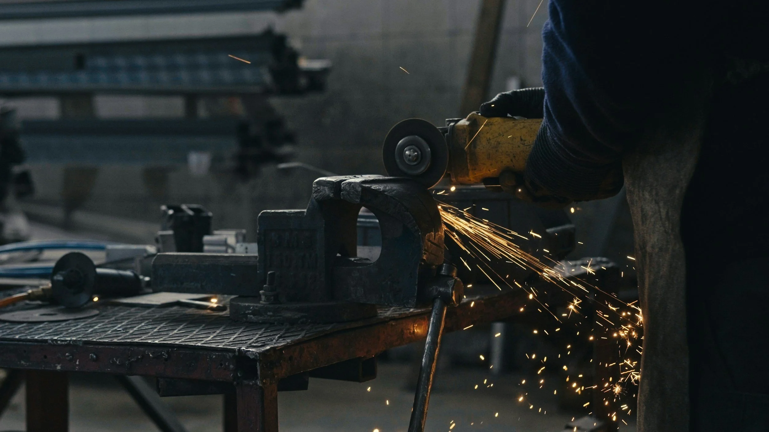 Person using a handheld angle grinder to cut metal on a workbench, with sparks flying.
