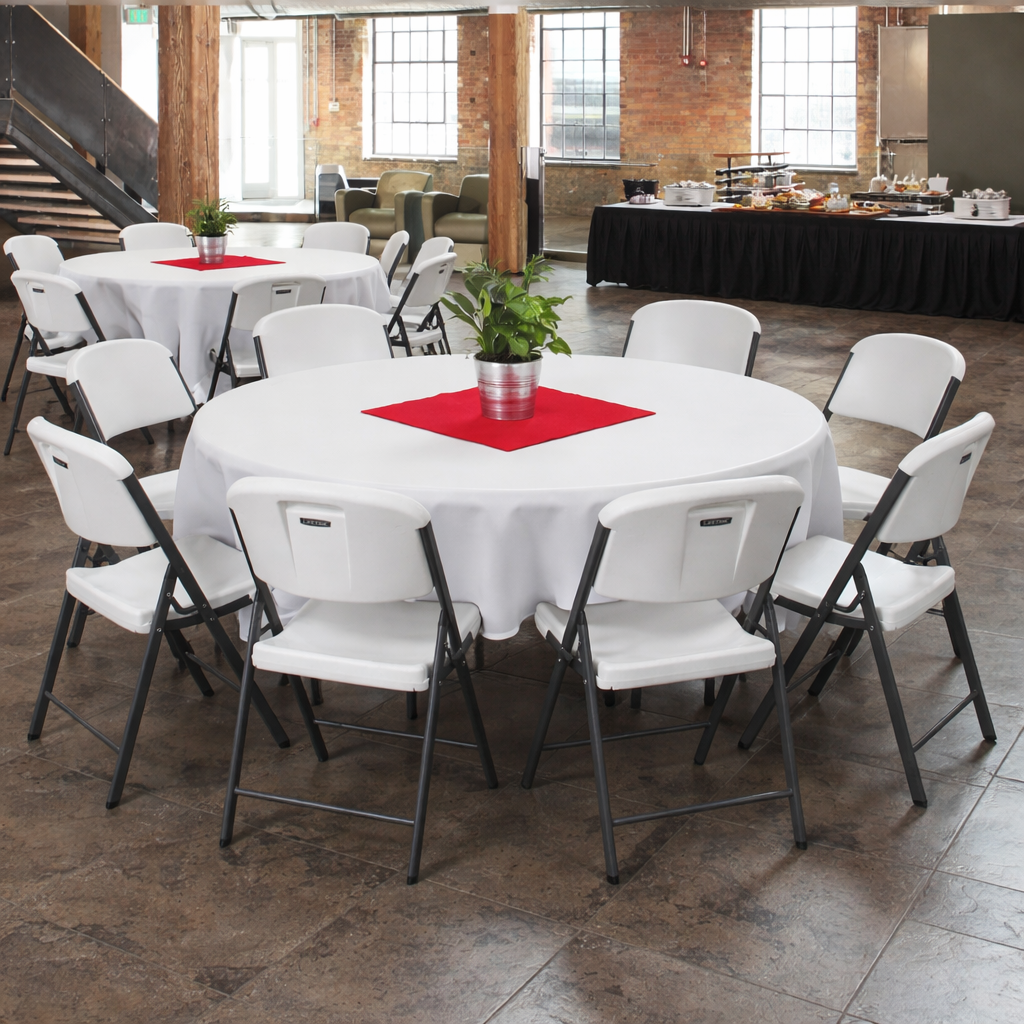 Indoor event space with round tables covered with white tablecloths, red placemats, and potted plants, set up for a gathering or conference, with a buffet table in the background.