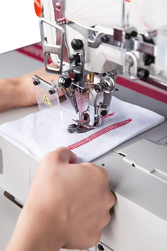 Seamstress sewing red thread on white fabric with industrial sewing machine.