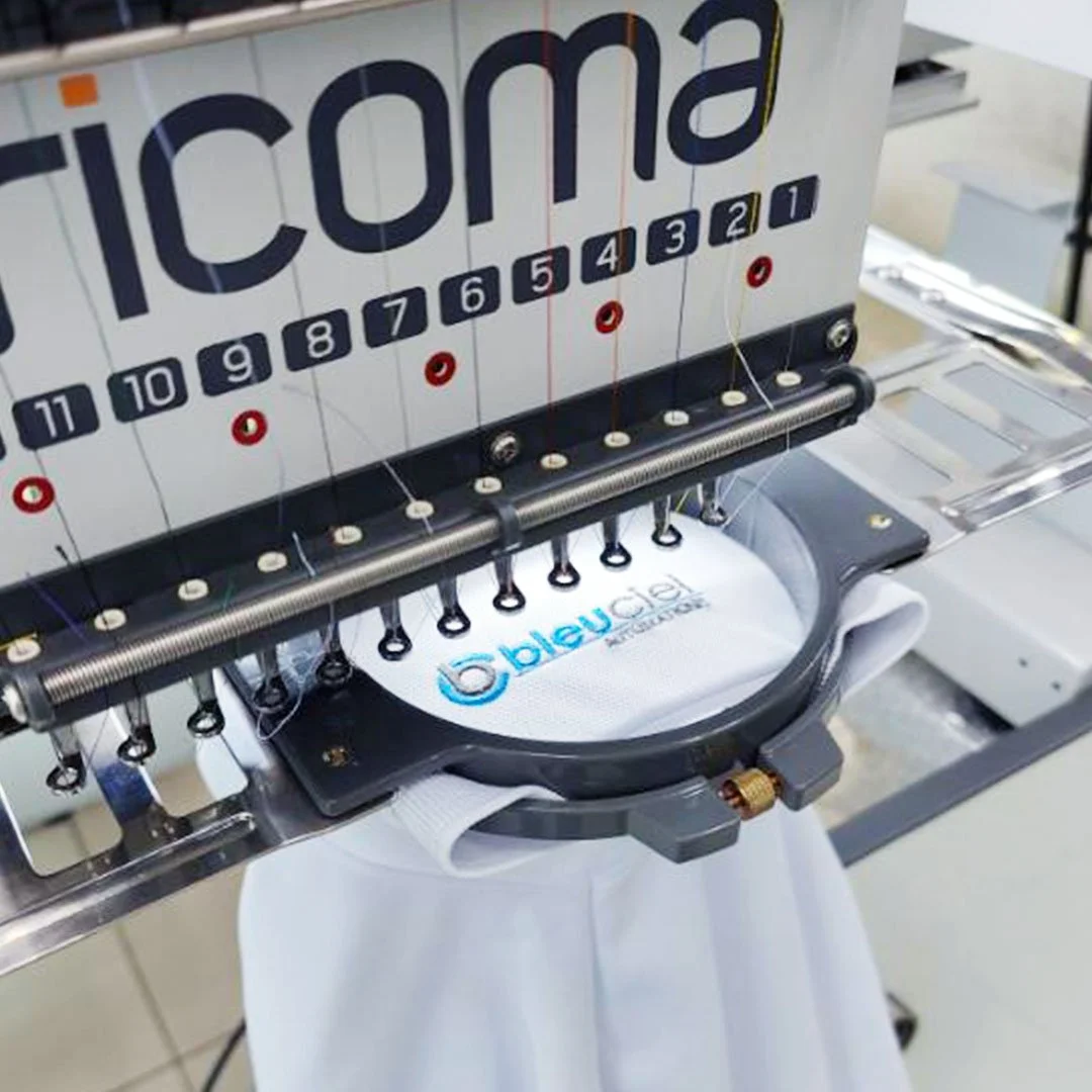 Embroidery machine stitching a white fabric with the Bleyle logo.