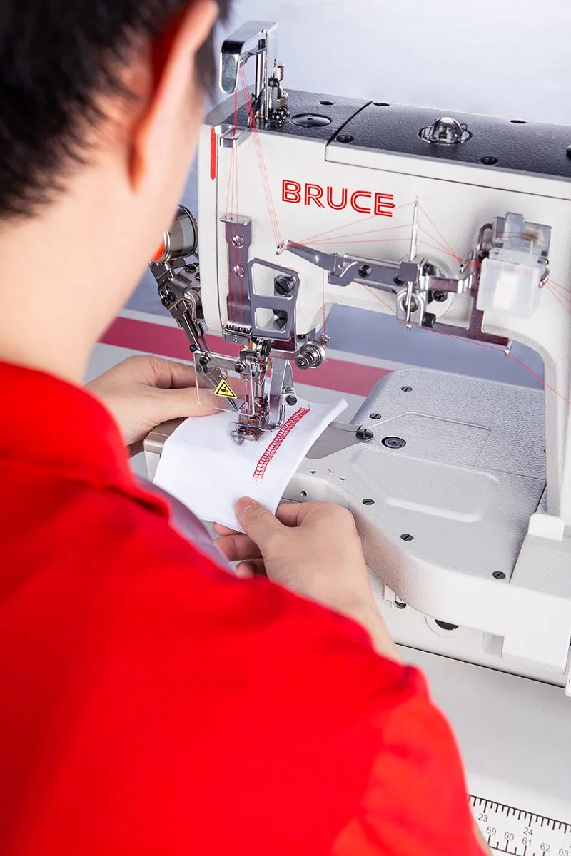 Person operating a sewing machine labeled 'BRUCE' while sewing white fabric.