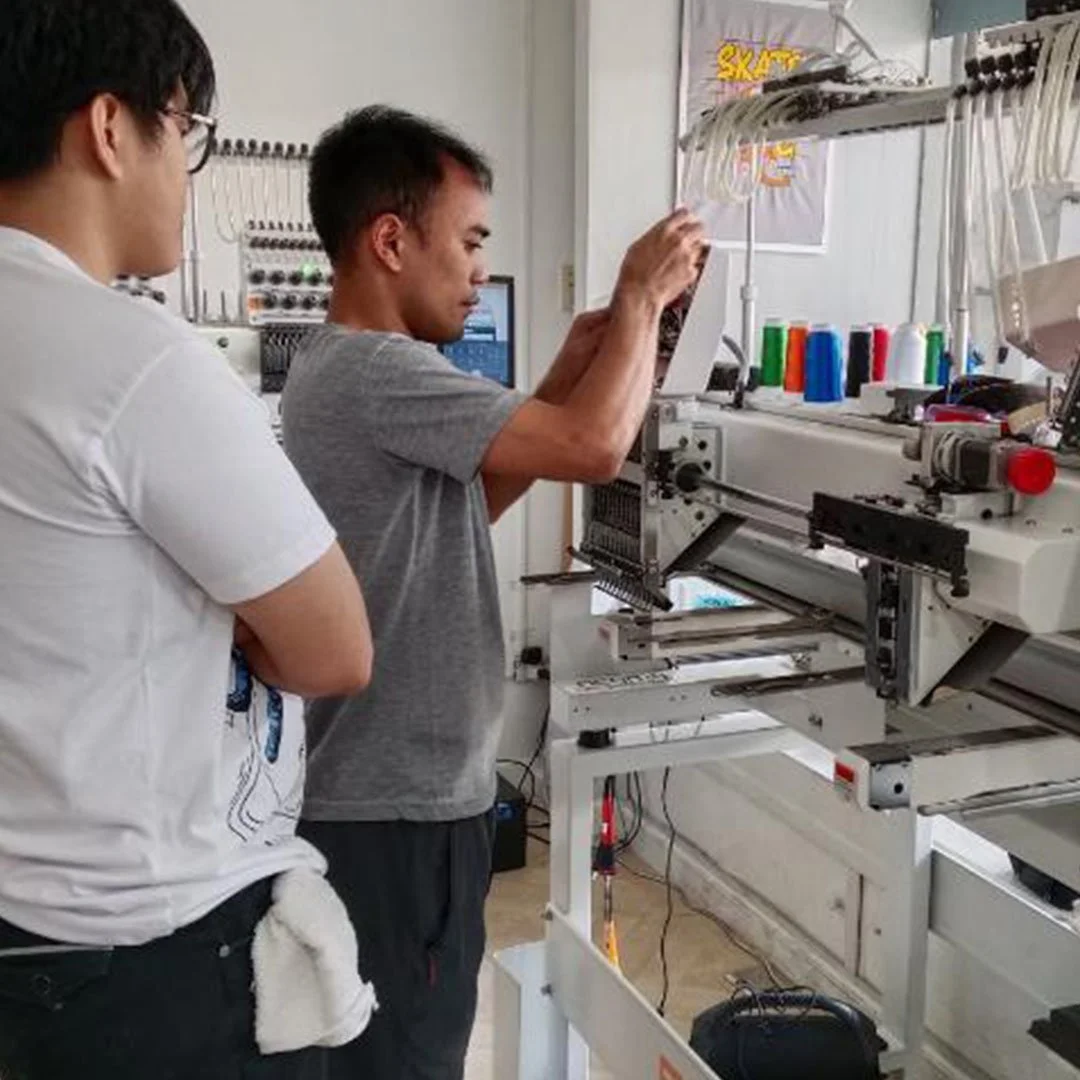Technician conducting industrial embroidery machine setup and training in a Philippine manufacturing workspace