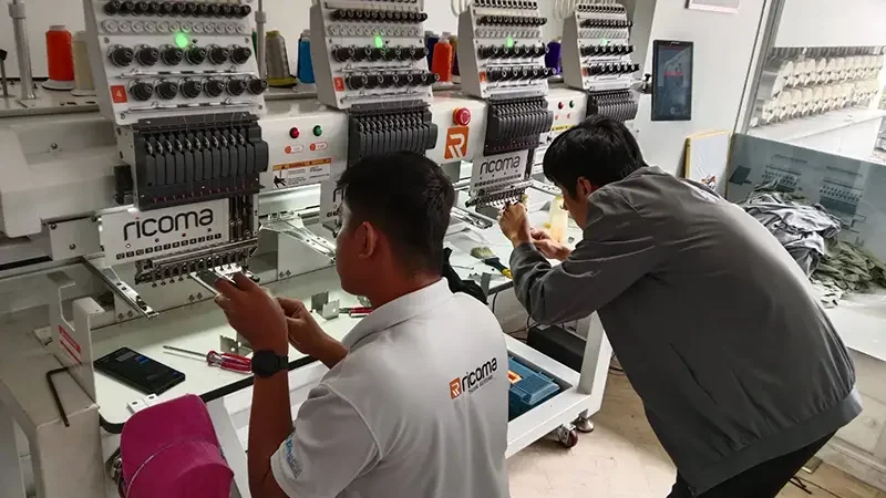 Bleuciel technicians conducting preventive maintenance on a Ricoma multihead embroidery machine