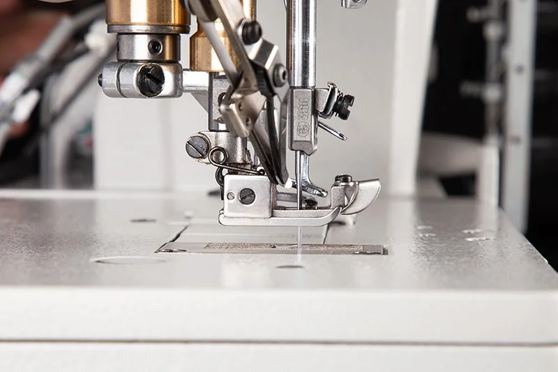 Close-up of a sewing machine needle and presser foot in a manufacturing or sewing workshop.
