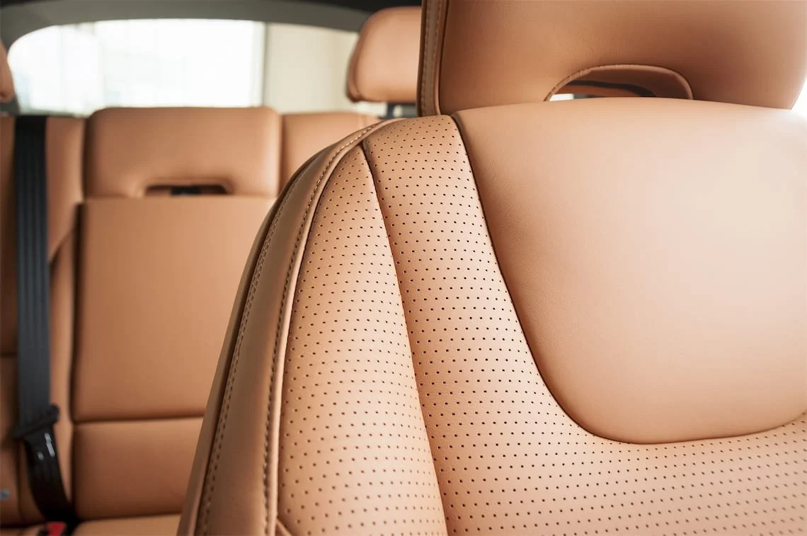 Close-up of tan leather car seats with perforations in the rear seat of an SUV.