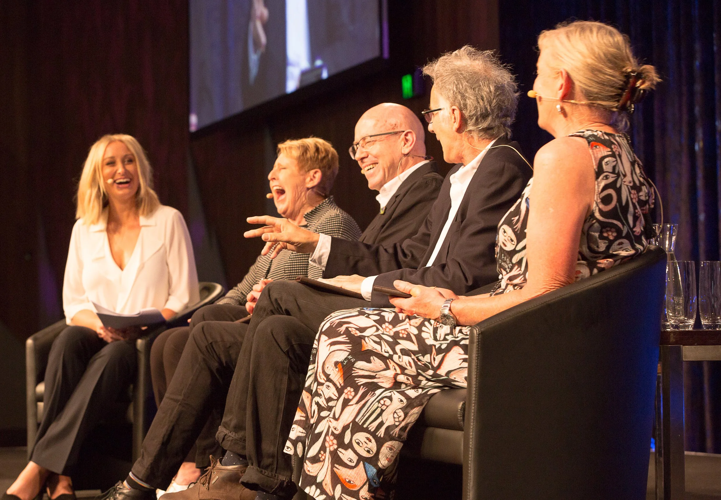 Jane Bunn hosting a panel discussion, laughing and engaging with each other, with a large screen behind them.