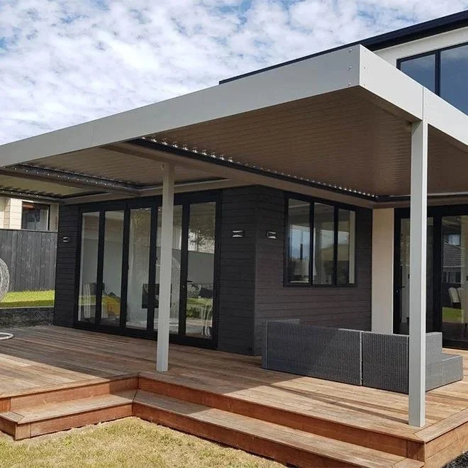Modern house exterior with a wooden deck and a covered patio area, featuring large glass sliding doors and black window frames.