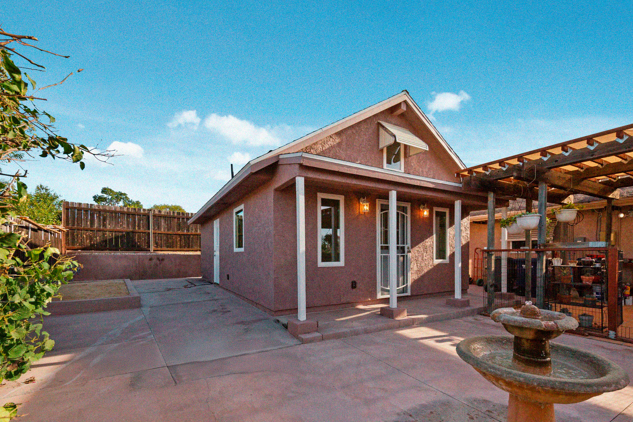 Casa de dos pisos con patio amplio, fuente en primer plano y cielo despejado.
