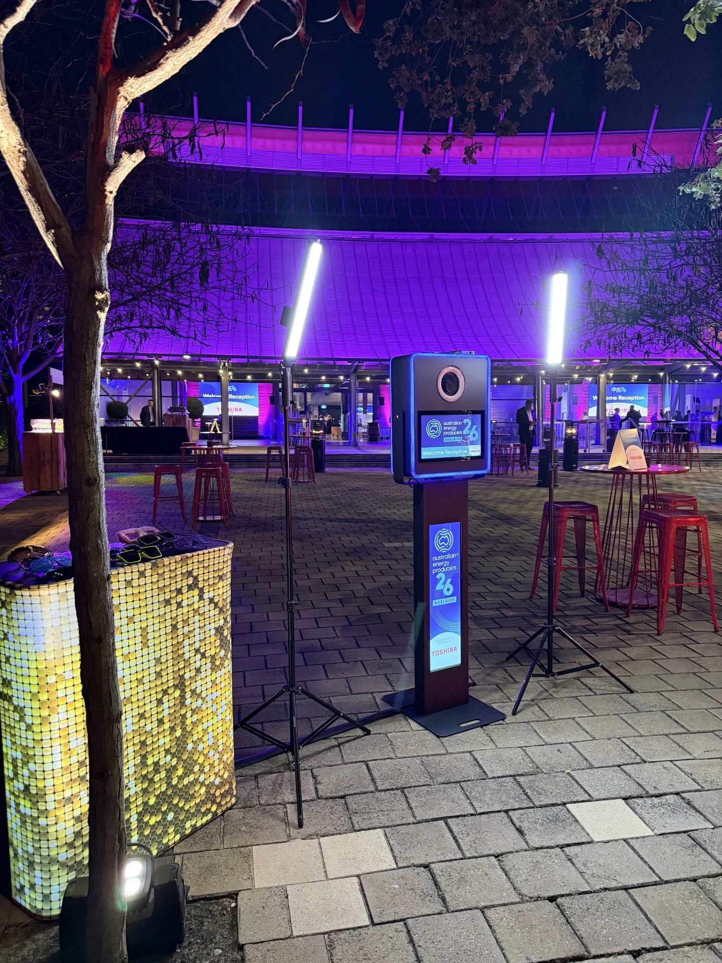 An outdoor event space at night with purple lighting, tables, chairs, and display boards for the Australian Energy Producers Adelaide event.
