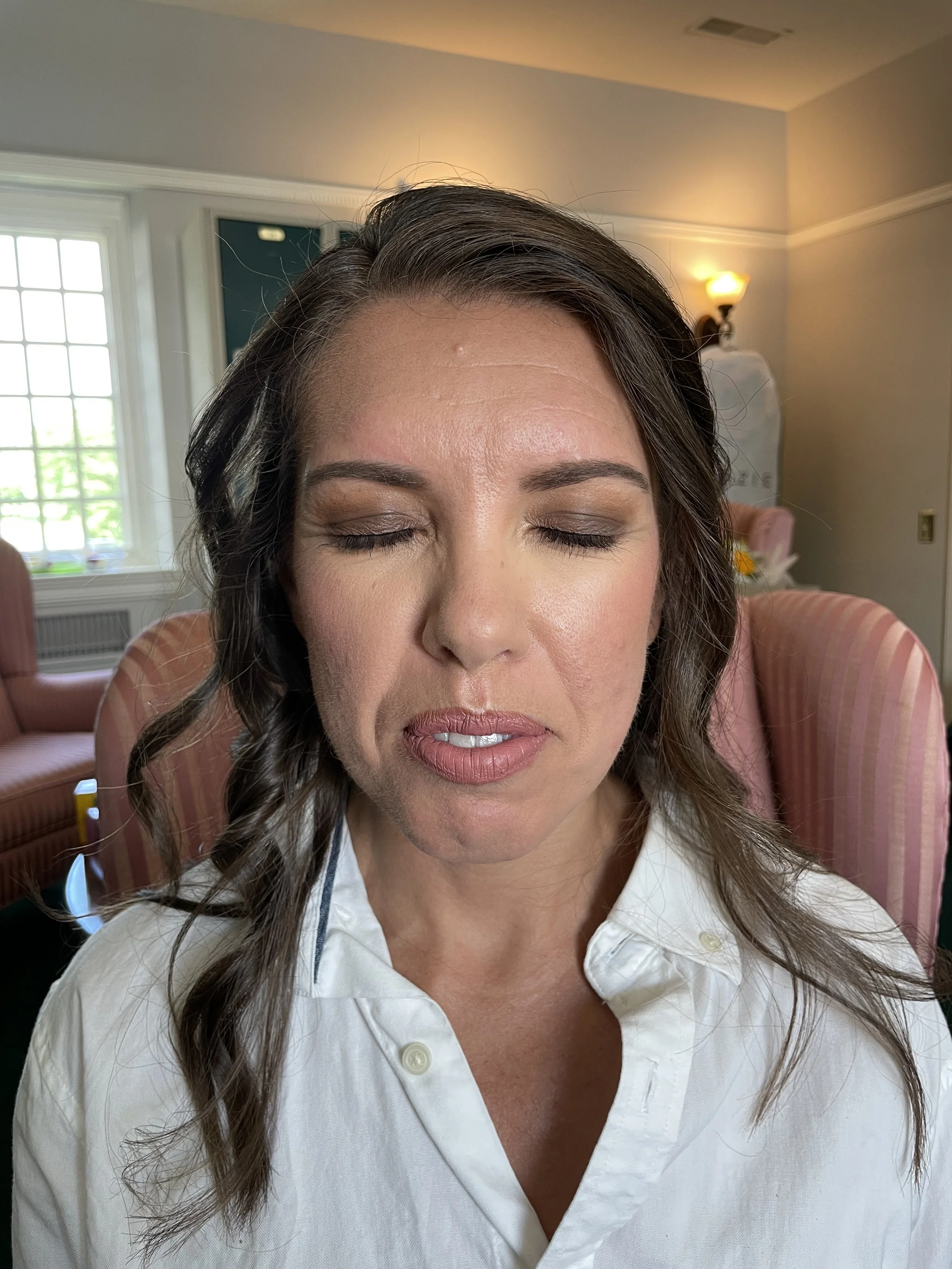 A woman with dark brown hair and closed eyes in a bright room with pink furniture.
