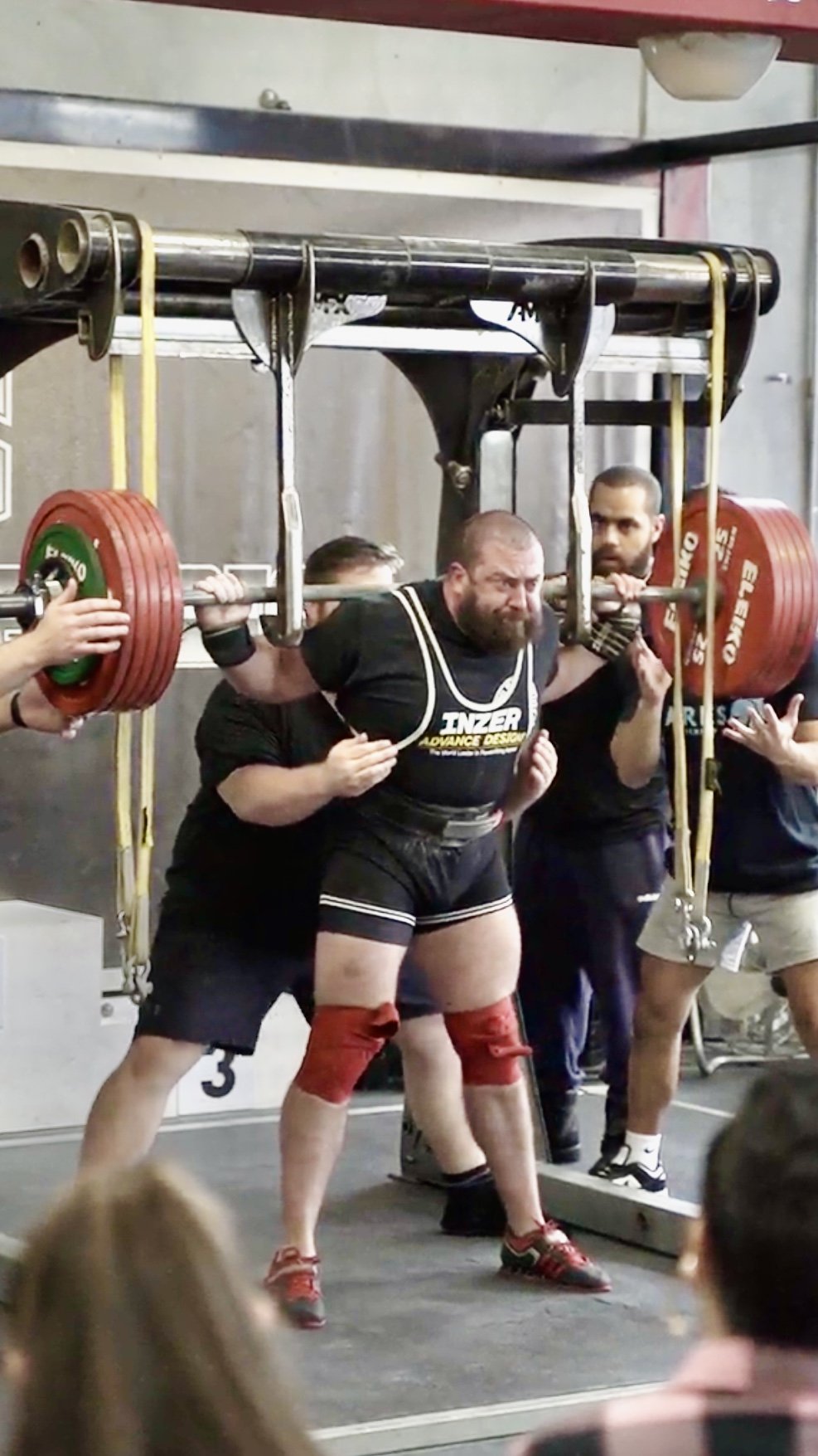A man in a weightlifting suit lifting a heavily loaded barbell during a powerlifting competition.