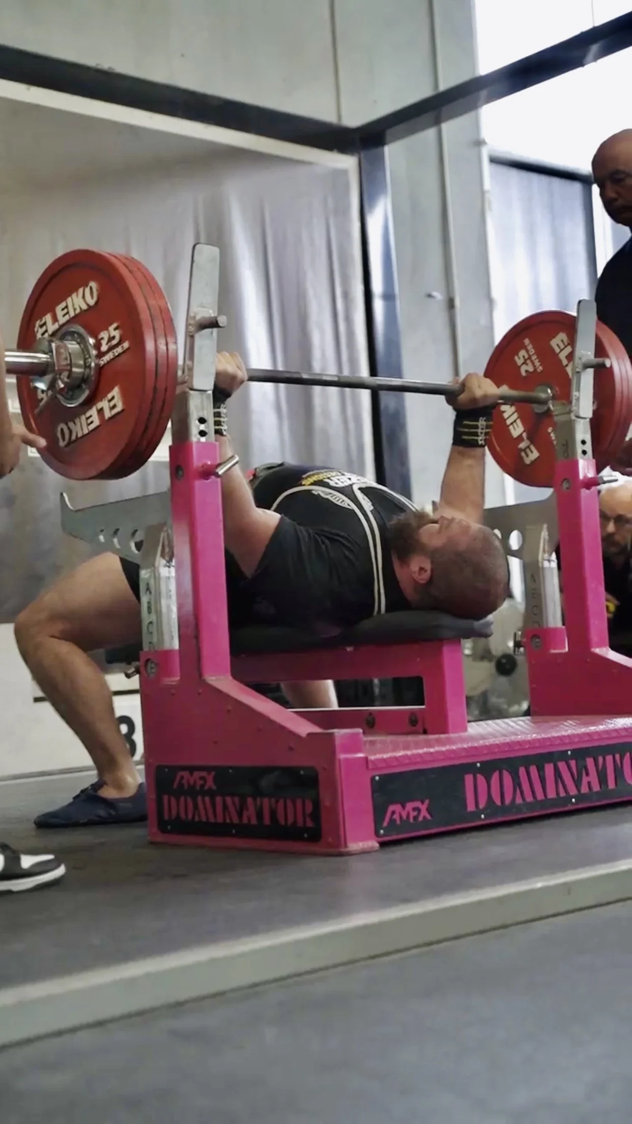 Man performing a bench press on a pink ADMAX Domination lifting bench with red weight plates in a gym.