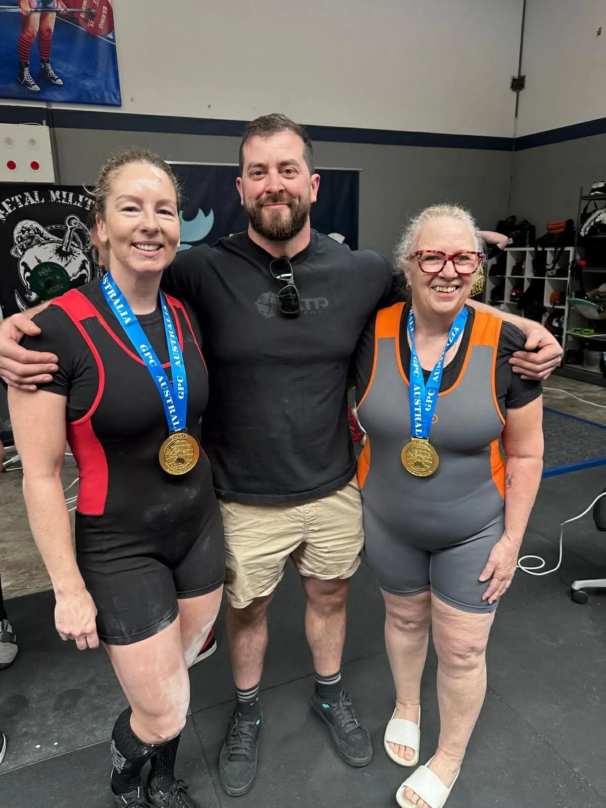 Three people standing together with medals around their necks in a gym, smiling at the camera.