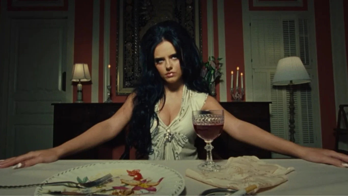 Jessie Murph sitting at a 1960s dining table in the 1965 music video.