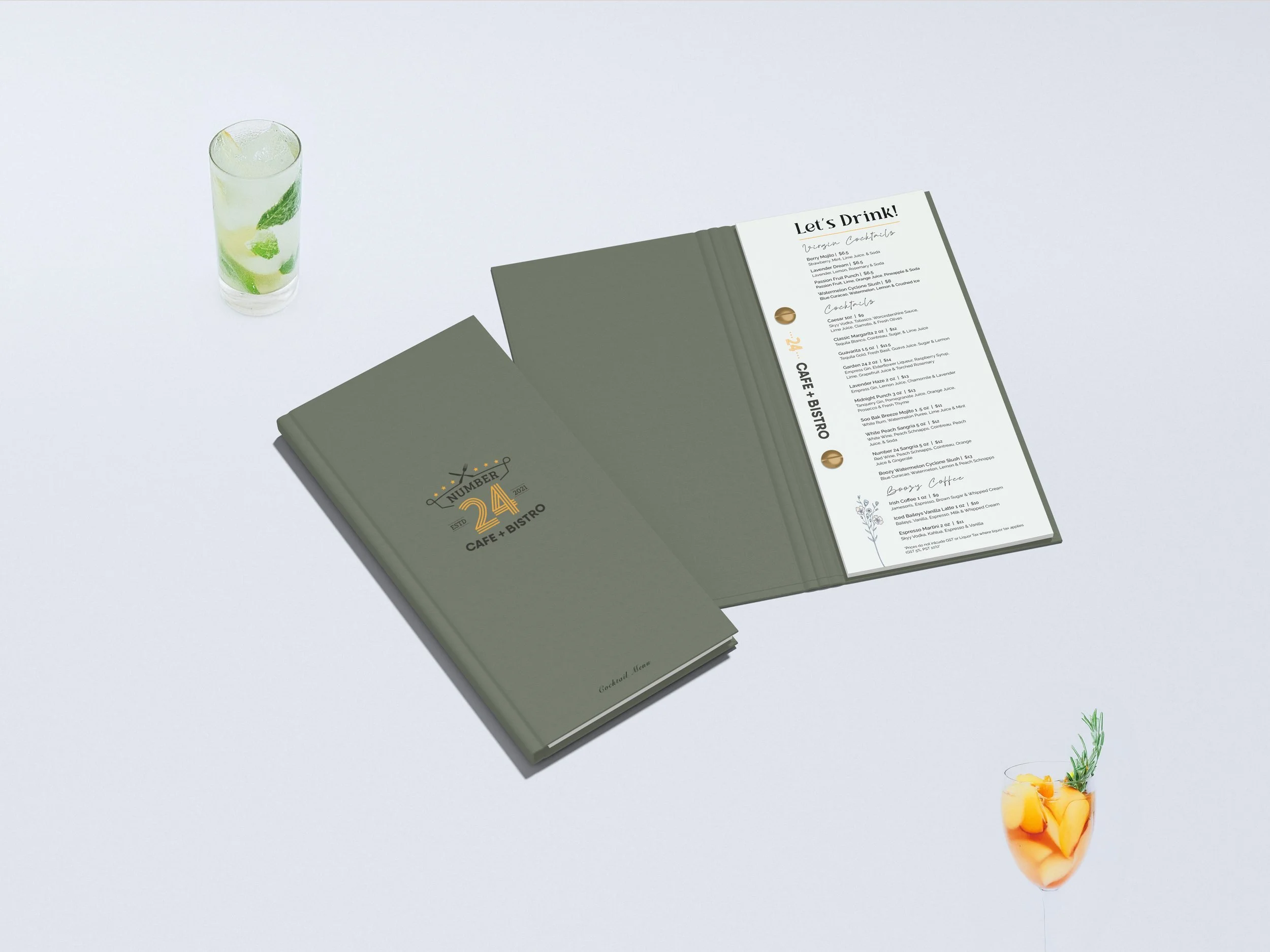 Two restaurant menus on a white table, one closed and one open, with a glass of lime and mint drink and a fruit cocktail.