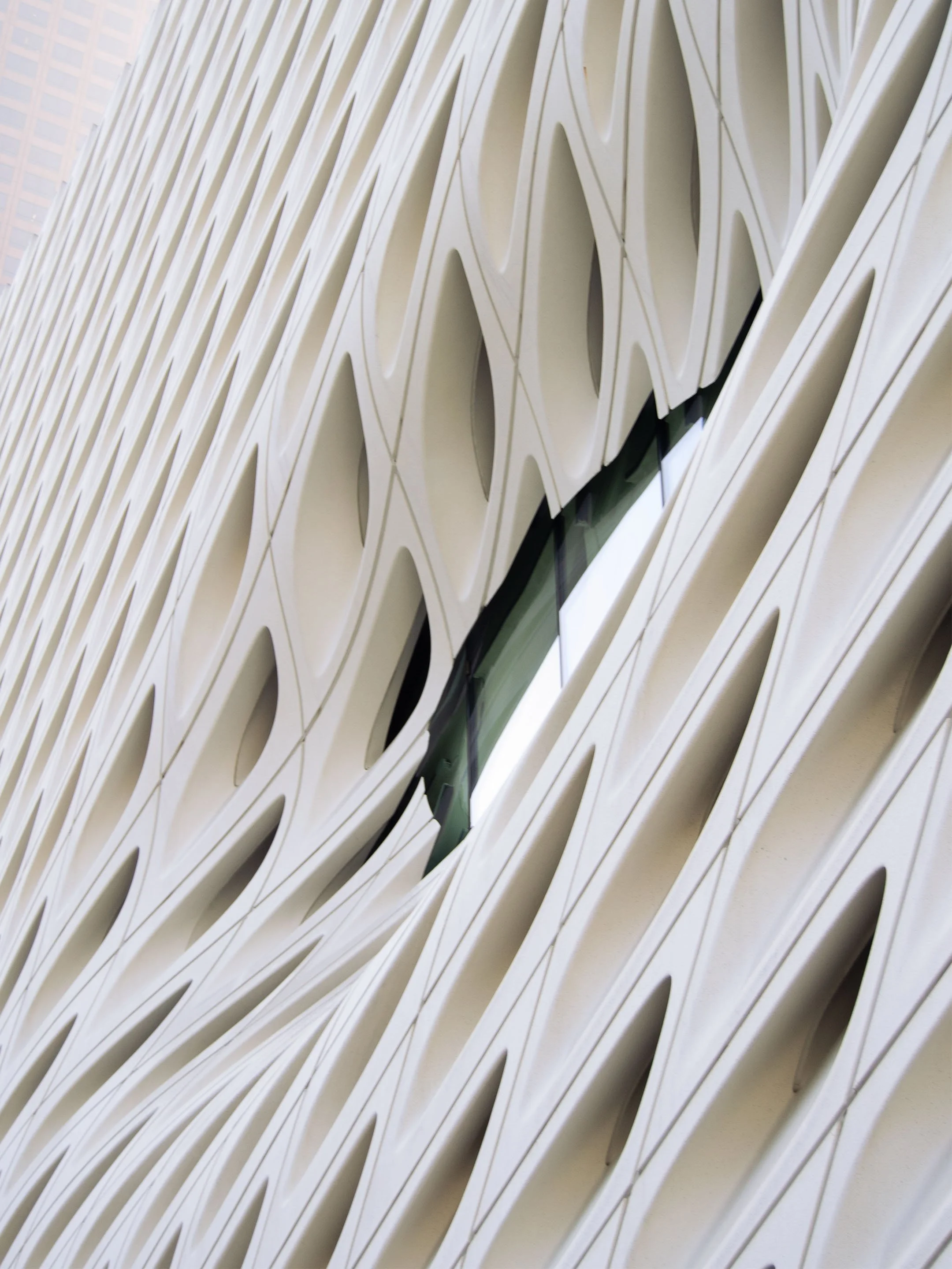 Close-up of a modern building facade with geometric, lattice-like white paneling and a small glass window reflecting the sky.