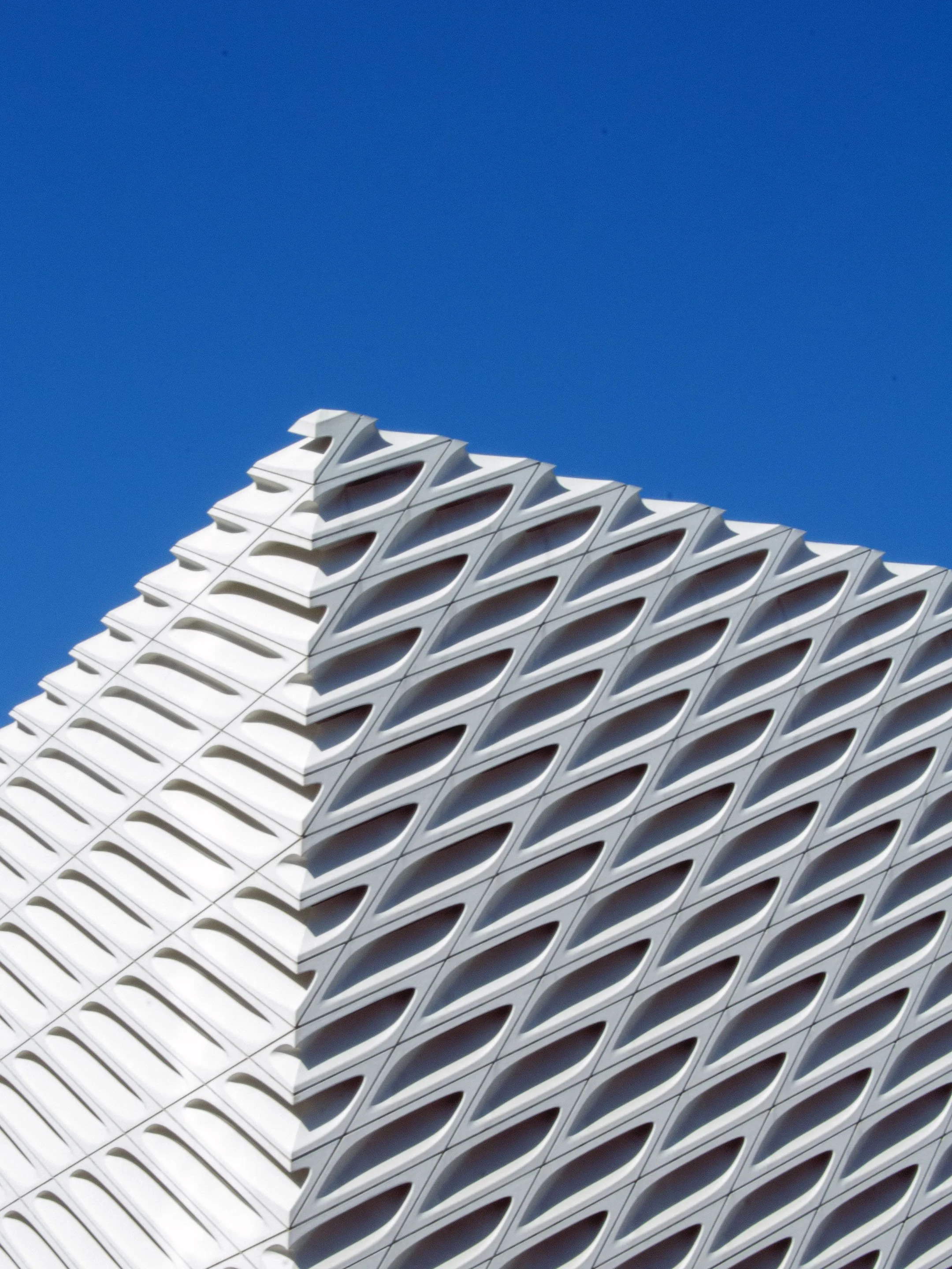 Modern architectural building with a white facade featuring a pattern of oval and rectangular openings, set against a clear blue sky.