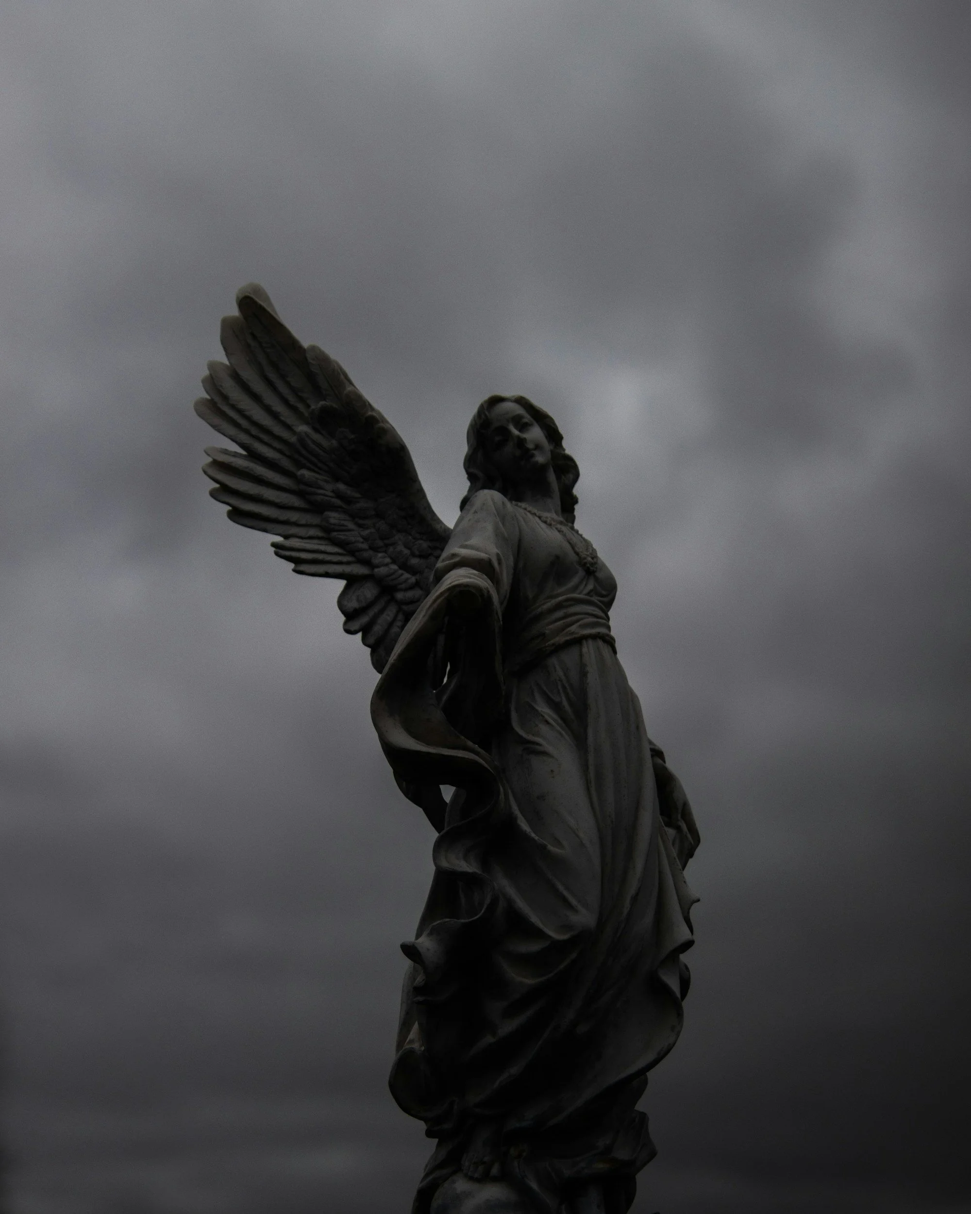 Statue of an angel with large wings against a cloudy sky.