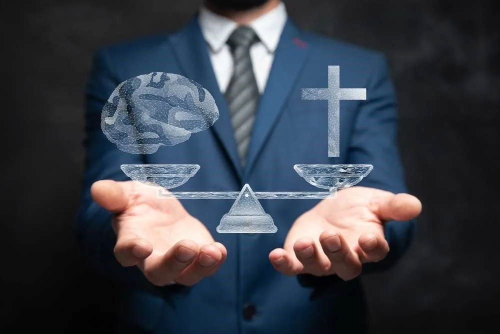 A man in a blue suit and striped tie holding out his hands, with digital illustrations of a brain and a cross balanced on a scale between them.