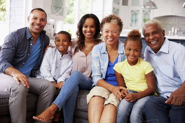 Multi-generational African American family smiling and sitting together on a couch in a bright living room.