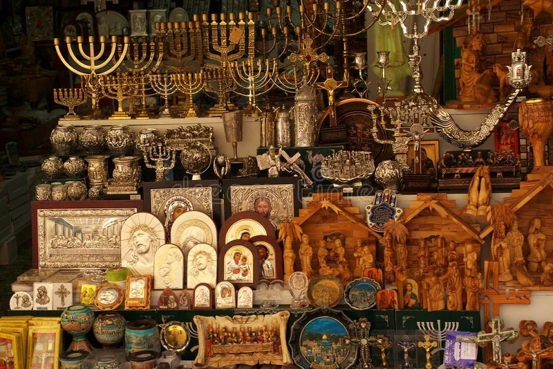 A display of various religious and cultural artifacts including menorahs, religious icons, wooden nativity scenes, crosses, and decorative boxes at a market or store.