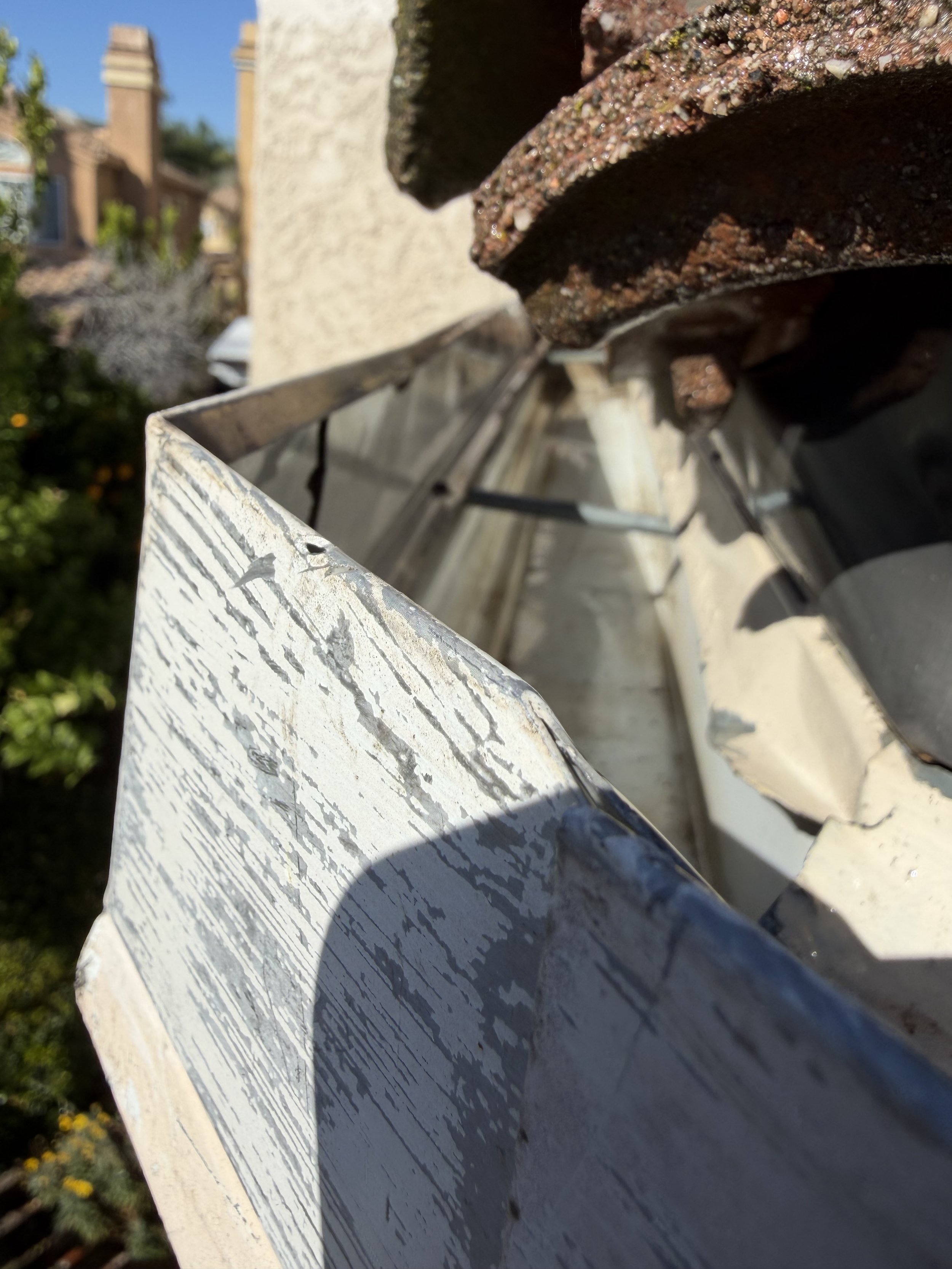 Close-up of a weathered, white wooden surface with peeling paint, a rusty metal pipe, and a textured, rust-colored brick wall in the background.