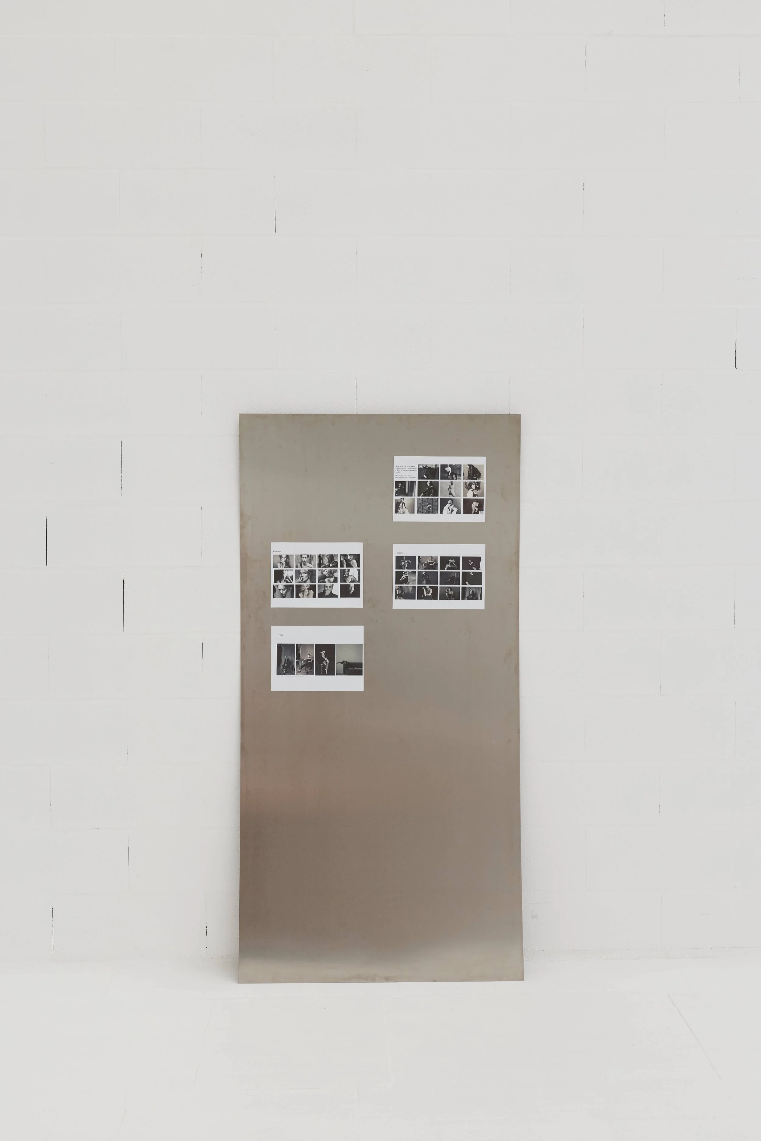 Panfleto de apresentação com várias fotos em preto e branco exibidas em uma parede de fundo cinza, posicionada na frente de uma parede branca.