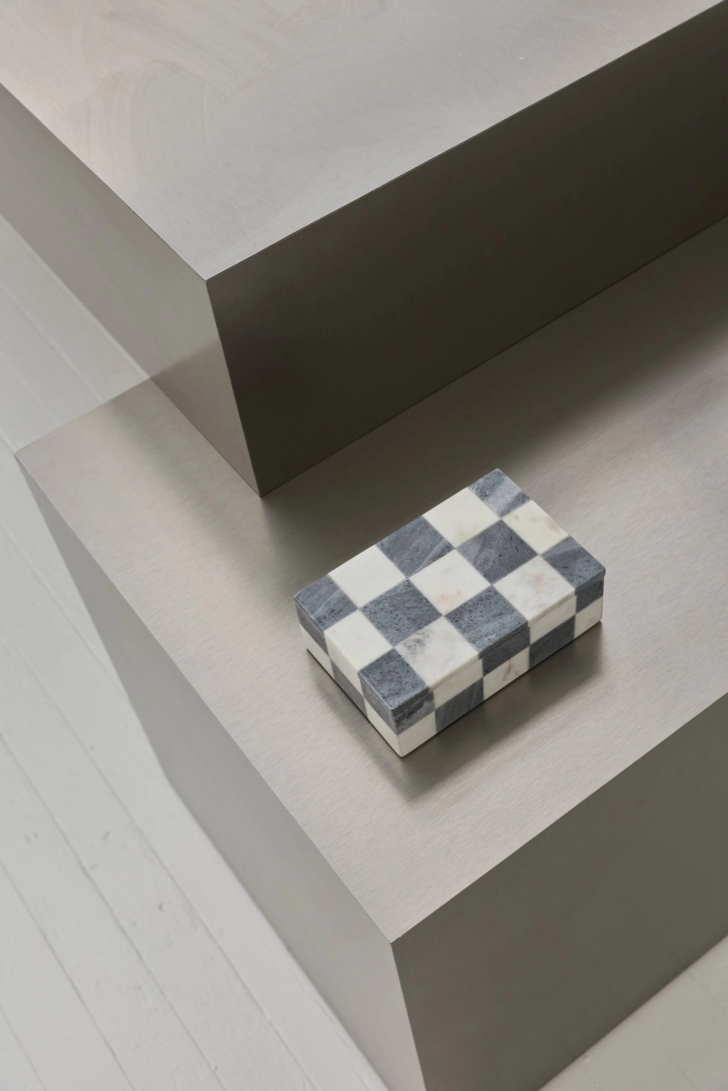 Imagem de uma mesa de canto com acabamento em cinza claro, com uma caixa decorativa de mosaico em preto e branco em cima.