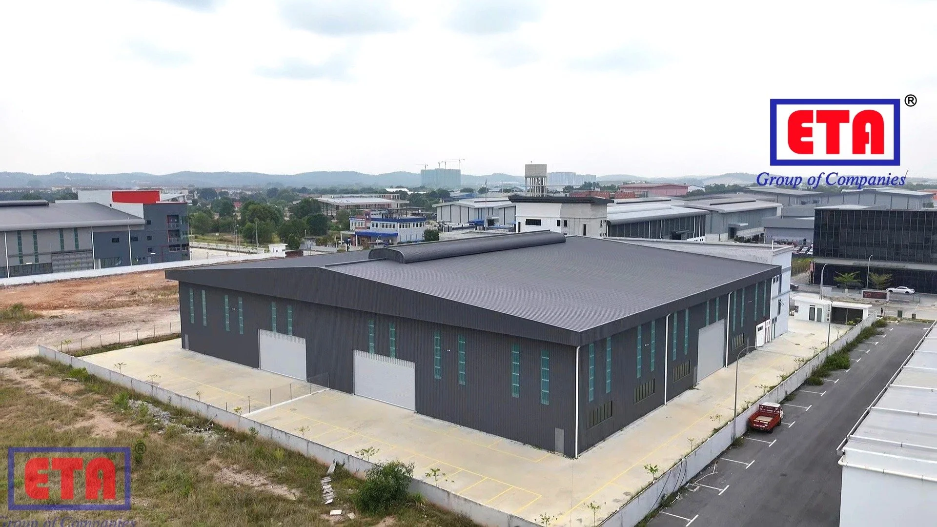 A large, modern industrial warehouse with a gray exterior, multiple overhead doors, and surrounding parking lot and open yard. The logo of ETA Group of Companies is visible in the top right corner.