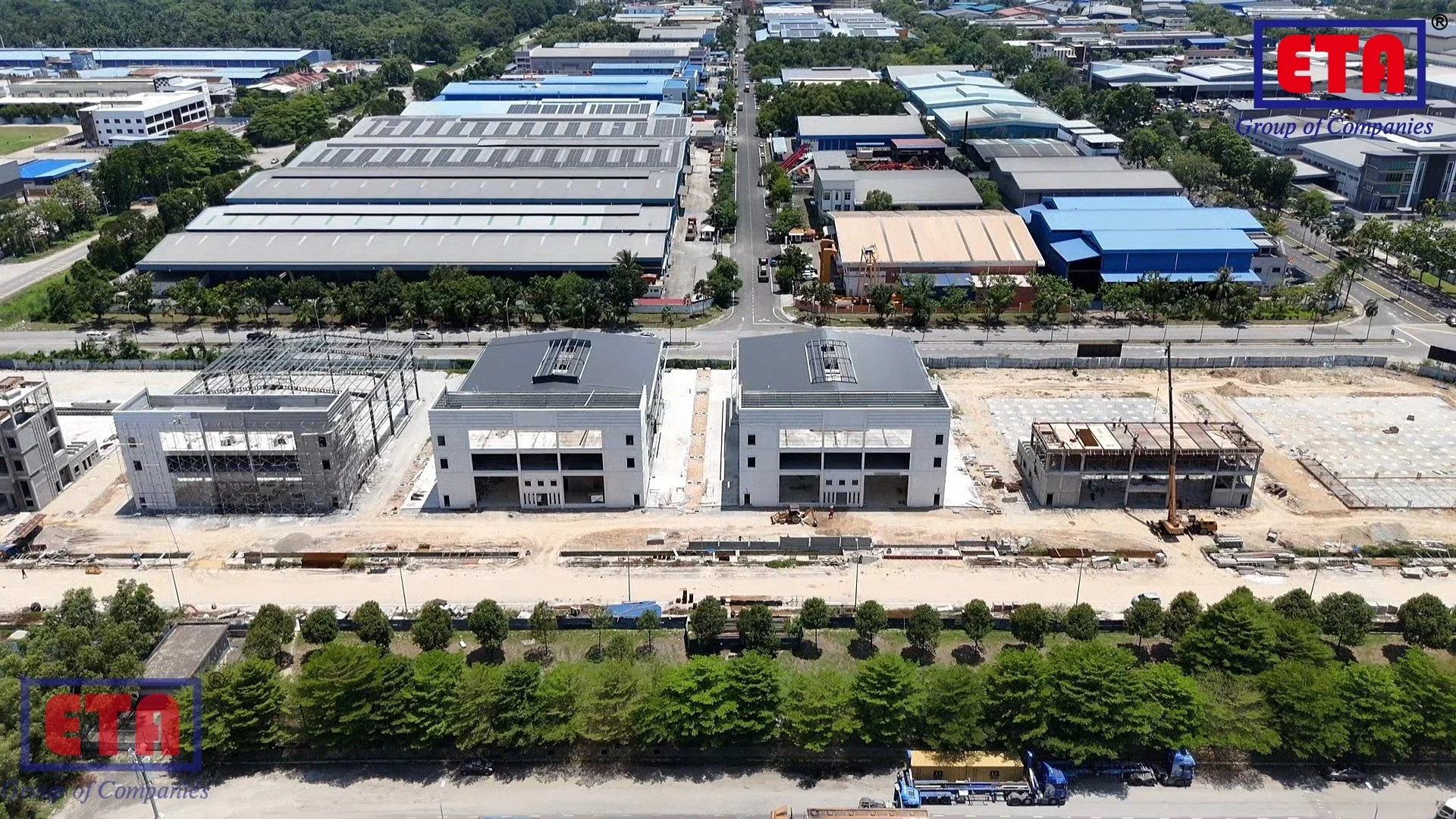 Aerial view of a construction site with two completed buildings in the foreground, construction in progress on nearby structures, surrounded by trees and roads, with industrial buildings in the background. The ETTA Group of Companies logo is at the top right corner.
