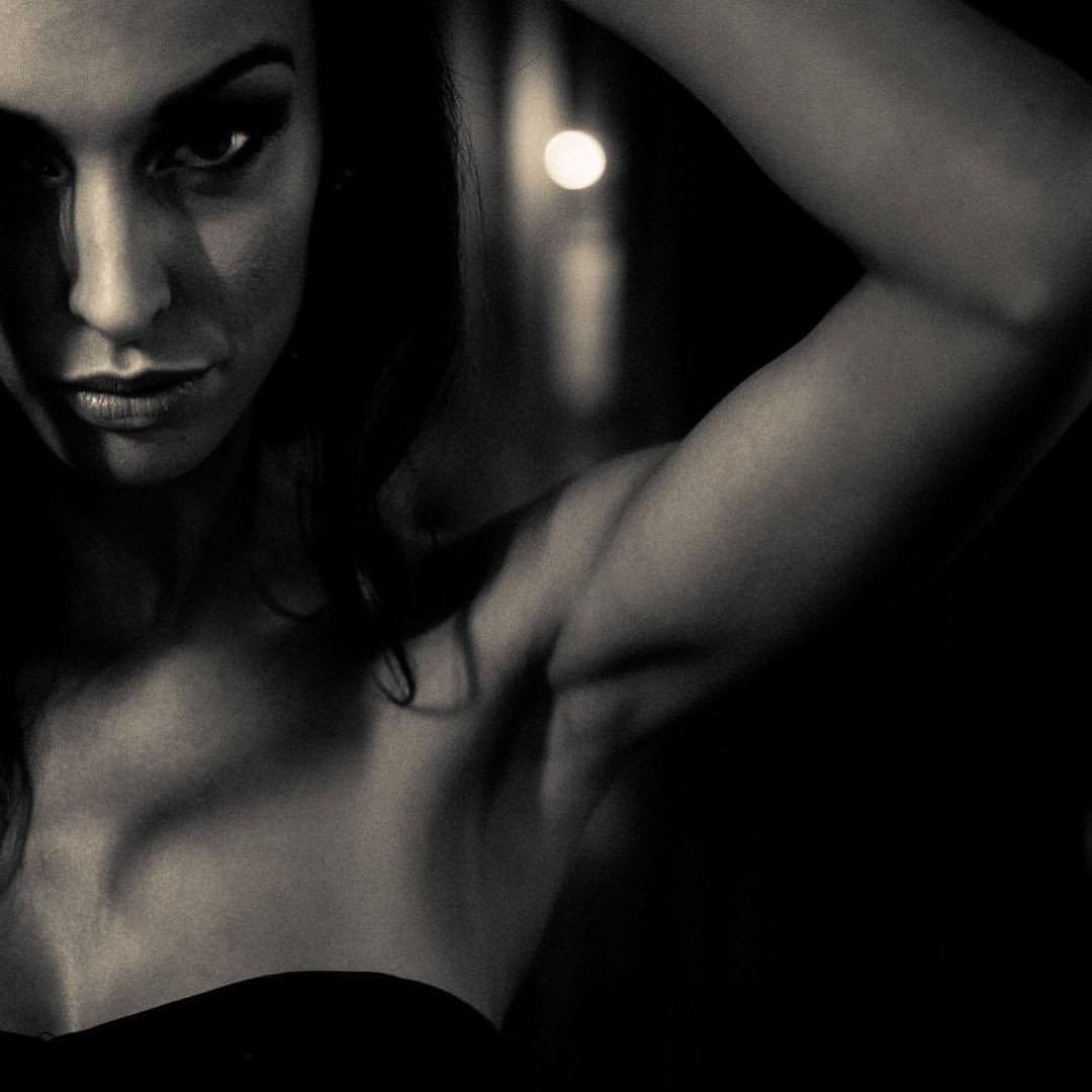 Black and white close-up image of a woman with intense expression, partially obscured face, and arms raised above her head.